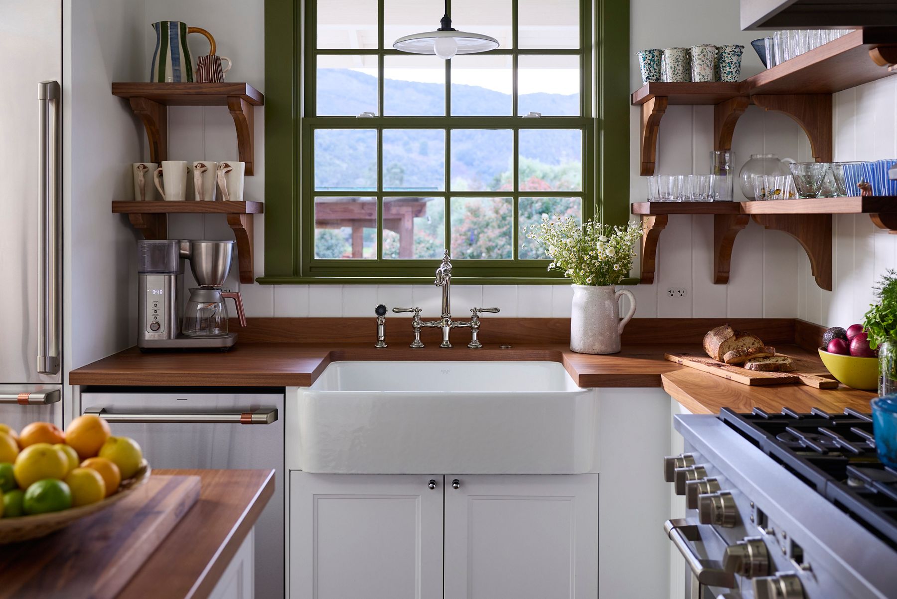 Cozy kitchen with a white farmhouse sink beneath a large window, wood countertops, floating shelves, and natural light.