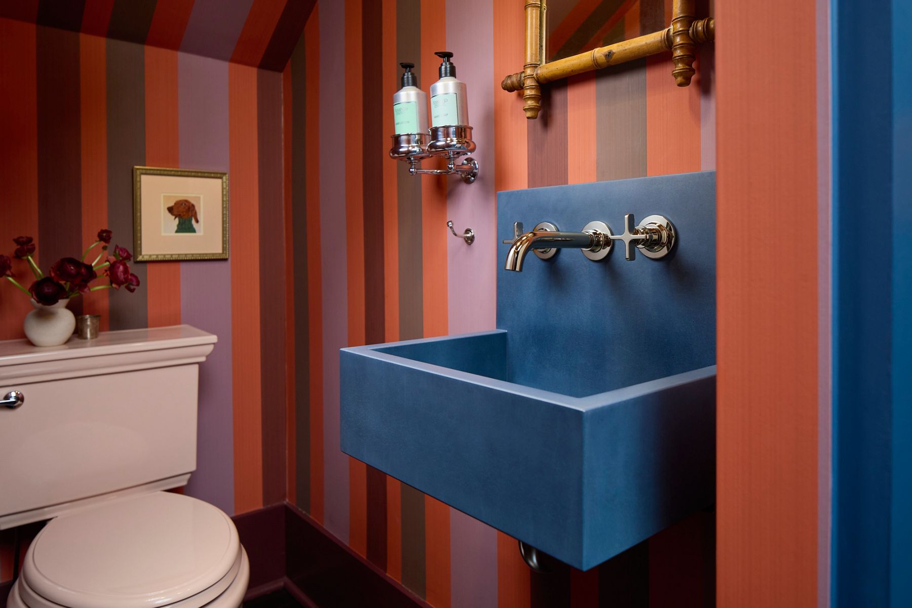 Bold powder room with red and orange striped walls, a sculptural blue wall-mounted sink, brass faucet, and dramatic lighting.