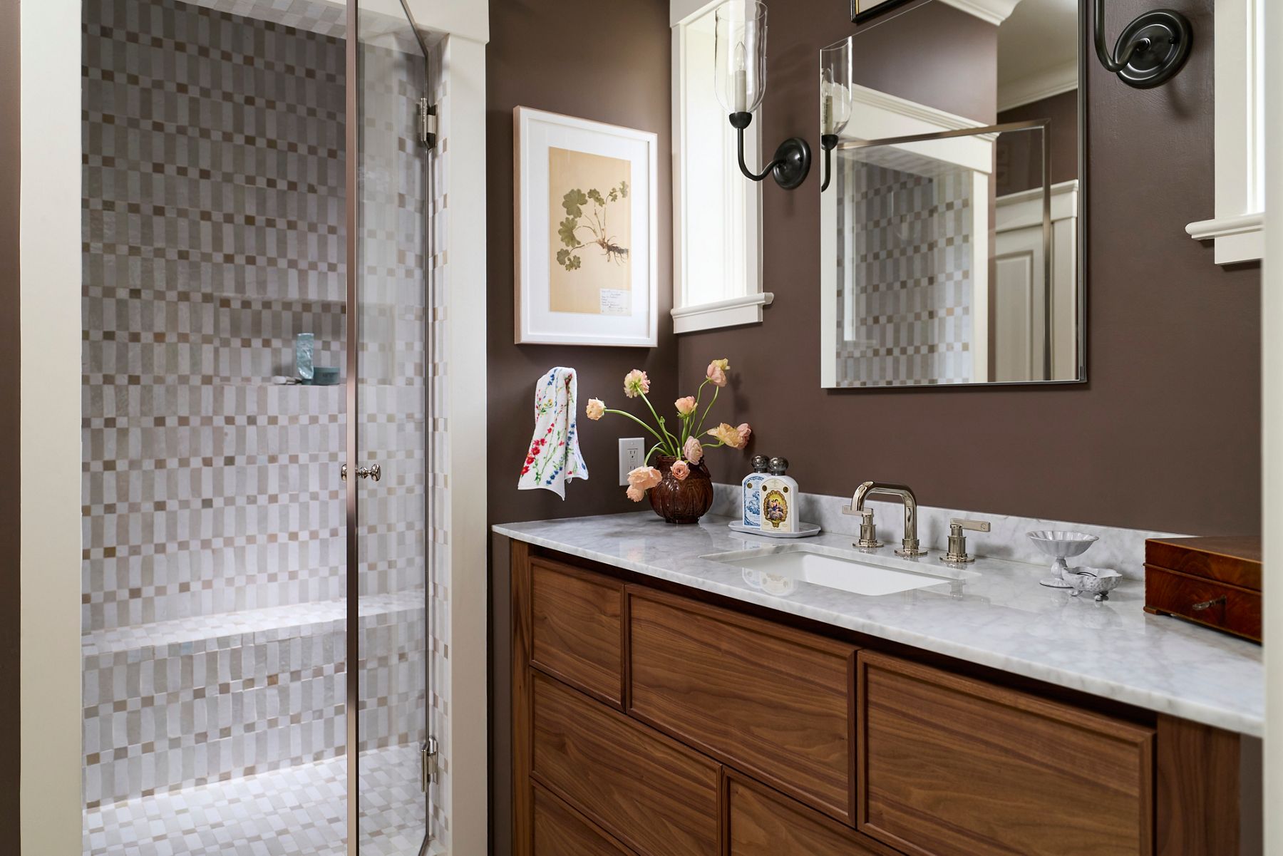 Contemporary bathroom with a wood vanity, marble countertop, walk-in tiled shower, and dark painted walls with framed artwork.