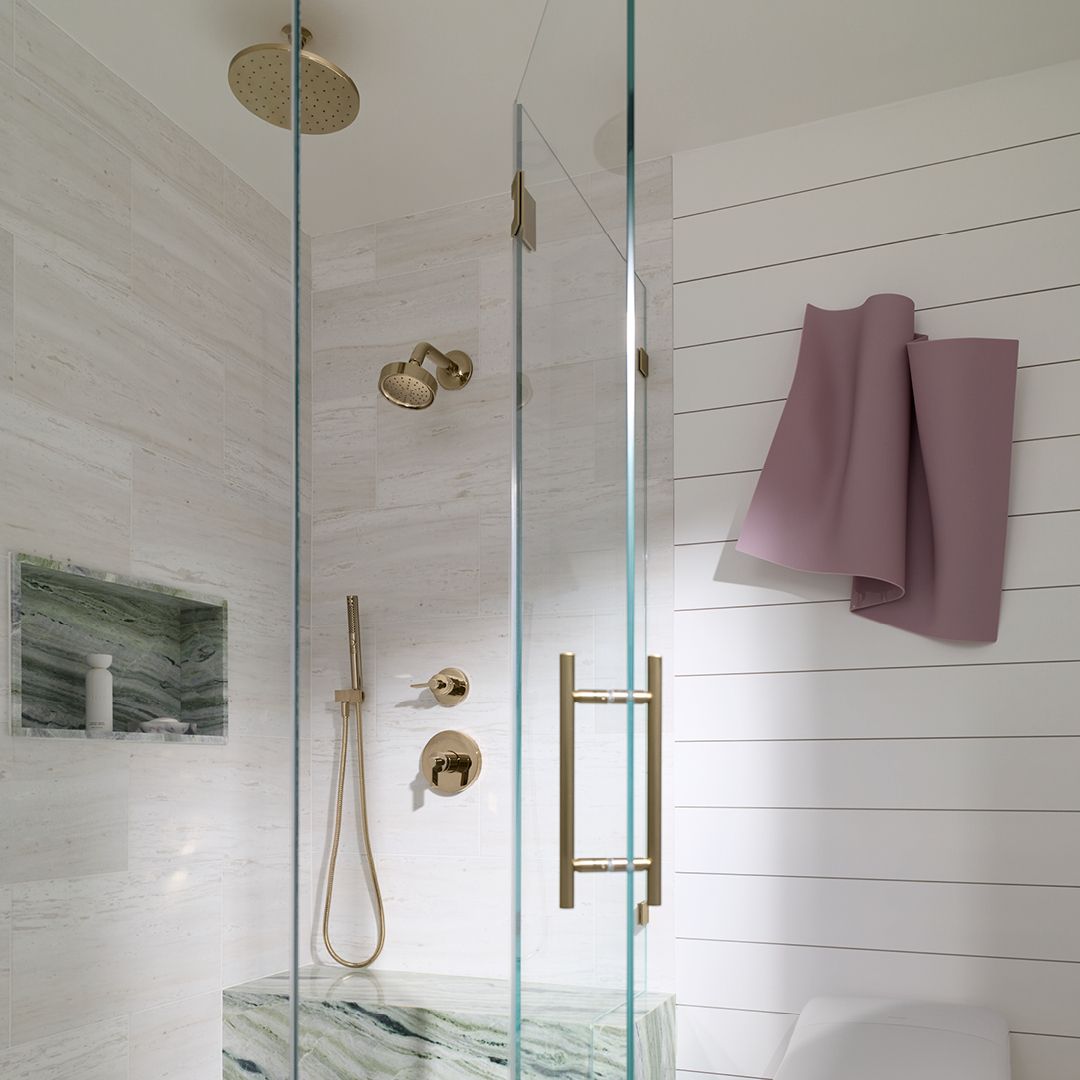 Glass-enclosed walk-in shower with brass fixtures, marble surfaces, and a built-in bench, with a towel hanging nearby.