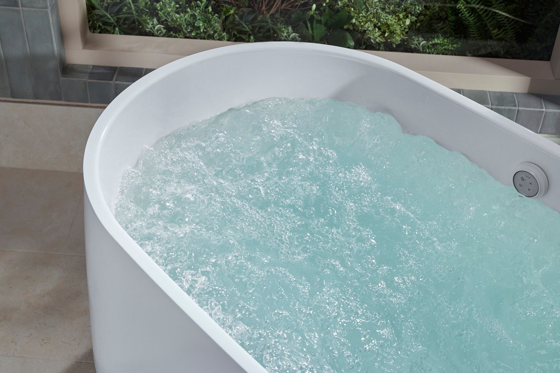 Close-up of a white freestanding bathtub filled with bubbling water, highlighting the hydrotherapy soaking experience and integrated overflow drain.