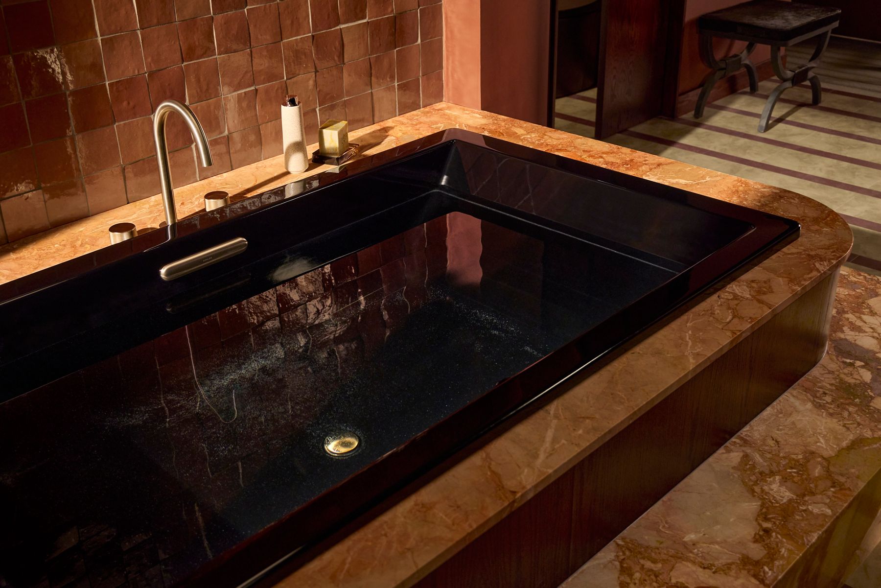 Rectangular black soaking bathtub set into a stone surround with a deck-mounted faucet, creating a luxurious indoor spa bathing experience.