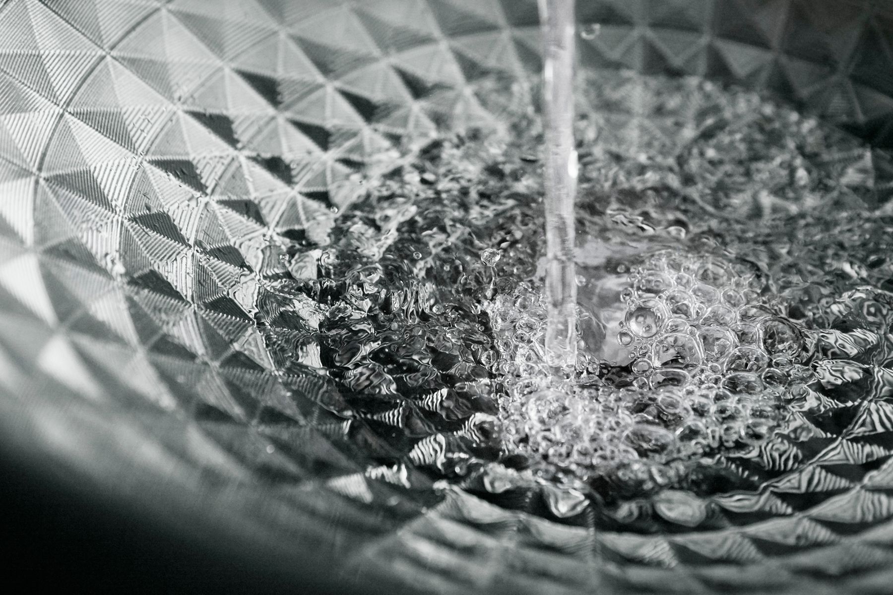 Close-up of geometric glass sink with running water