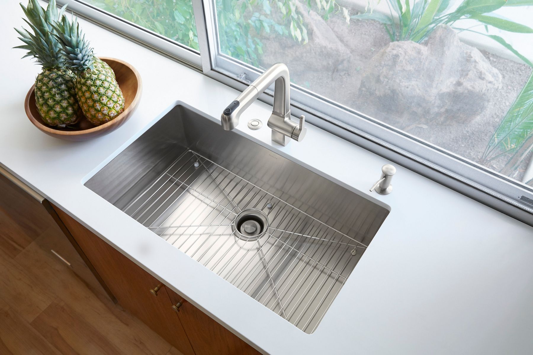 An undermount stainless steel kitchen sink with sharp 90-degree angles on the sides and bottom with a stainless steel faucet and light gray countertop.