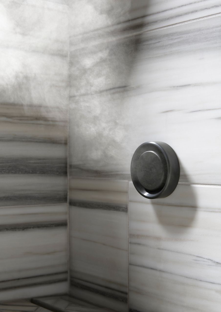 Gros plan d’une buse à vapeur émettant de la vapeur, montée sur un mur en pierre carrelée avec des stries horizontales gris clair, gris foncé et brun clair.