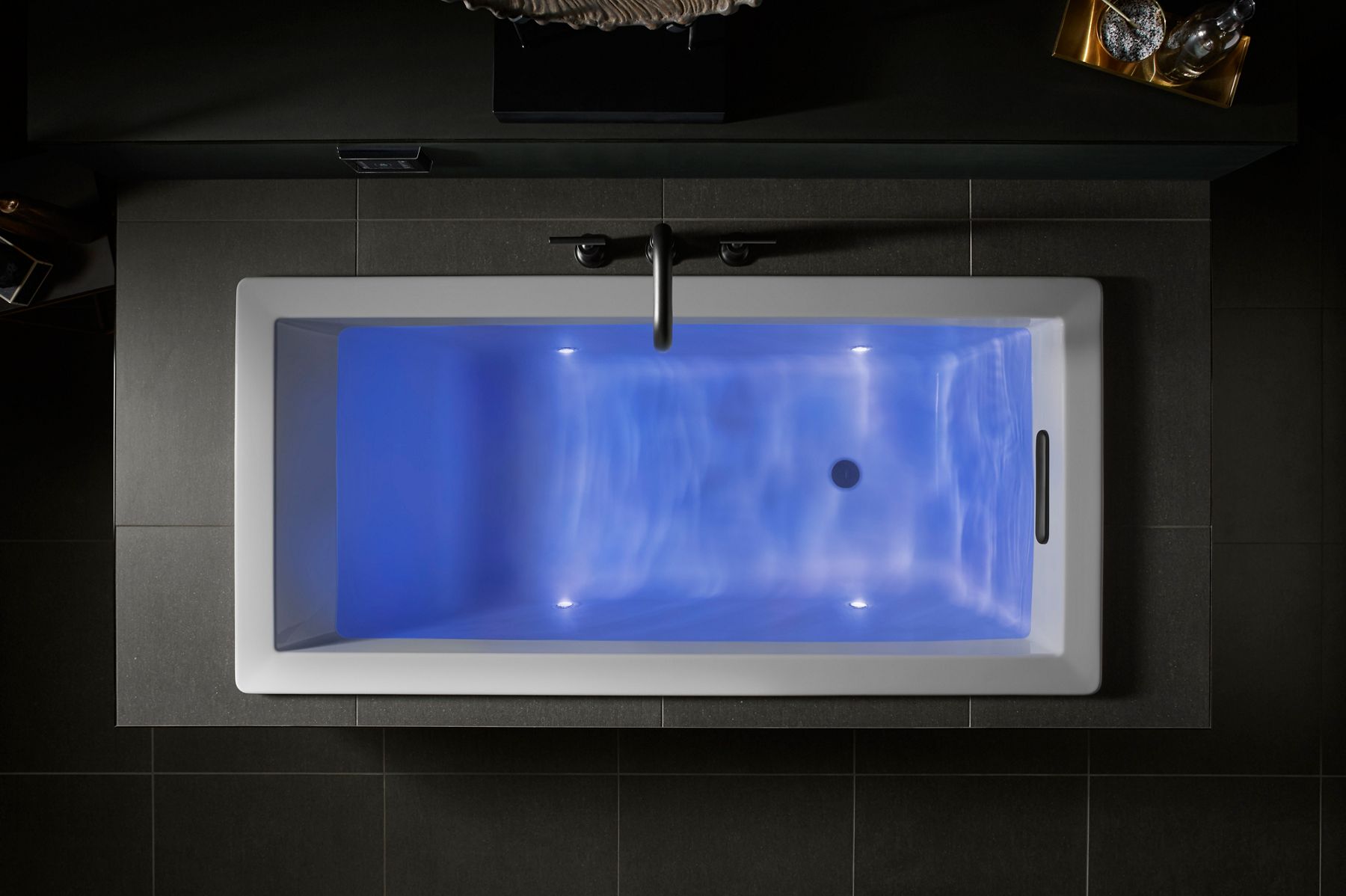 Overhead image of a KOHLER bath filled with water that's still and calm, illuminated by soothing blue lights from within the bath.