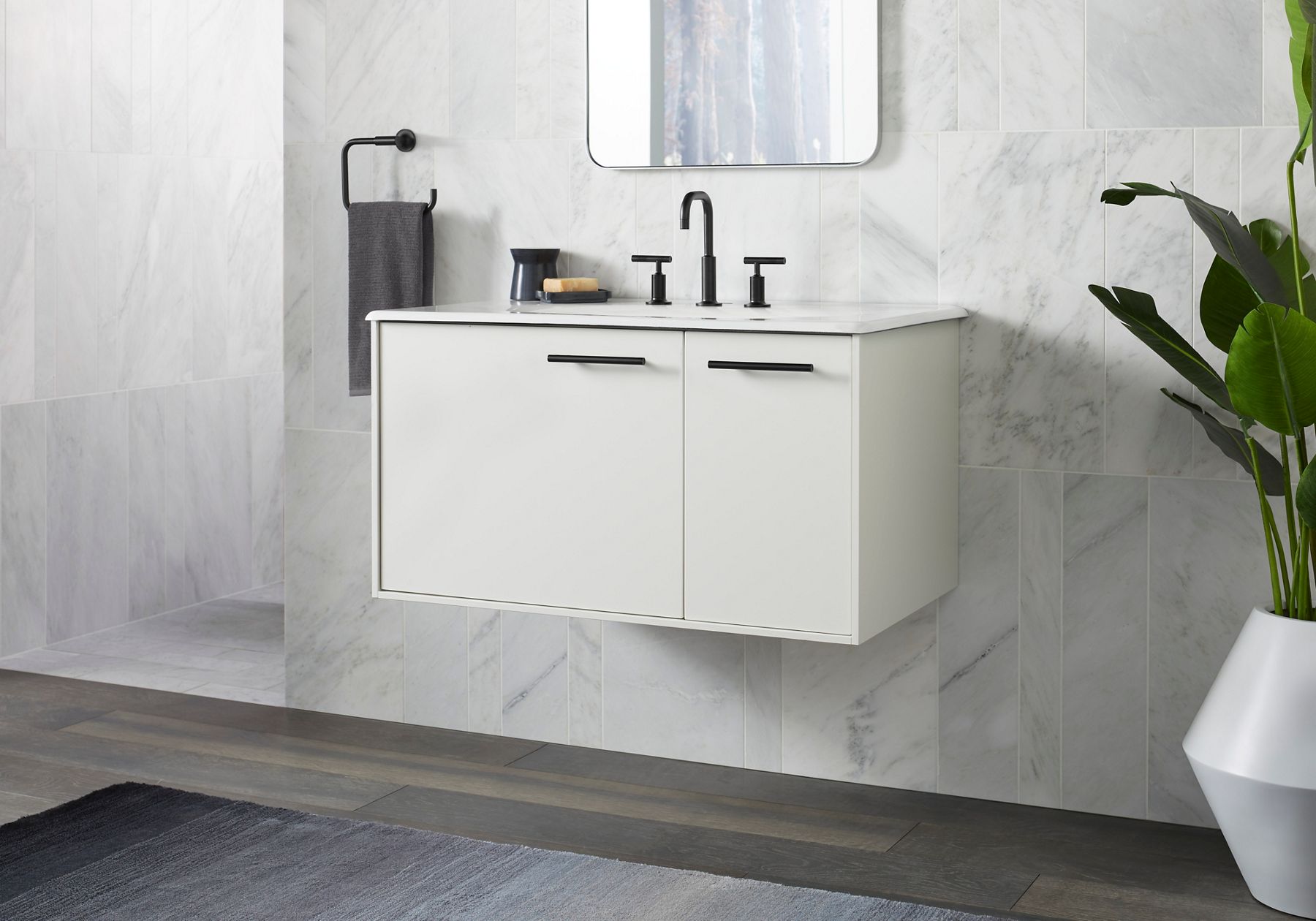 A white bathroom vanity with black hardware and a black widespread faucet against a white a wall with a mirror on it.
