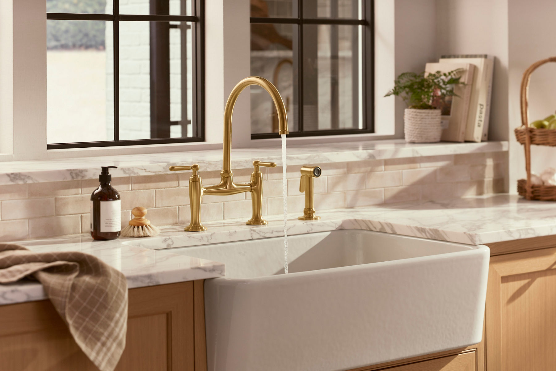 Golden-brass faucet on a marble countertop in a bright kitchen, promoting Kohler's water-saving design.