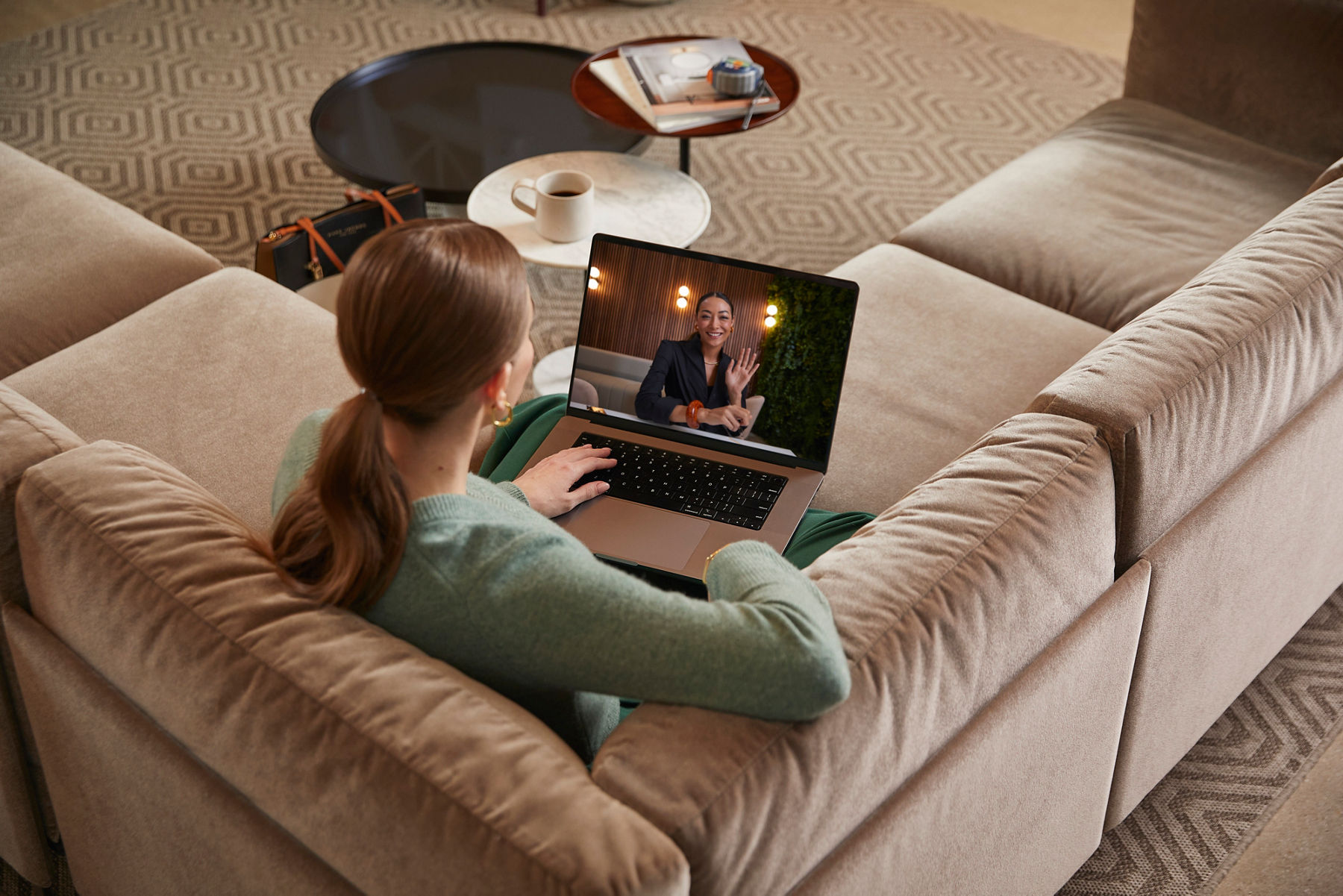 A woman sitting on a sofa holding a laptop, having a video call with a designer.