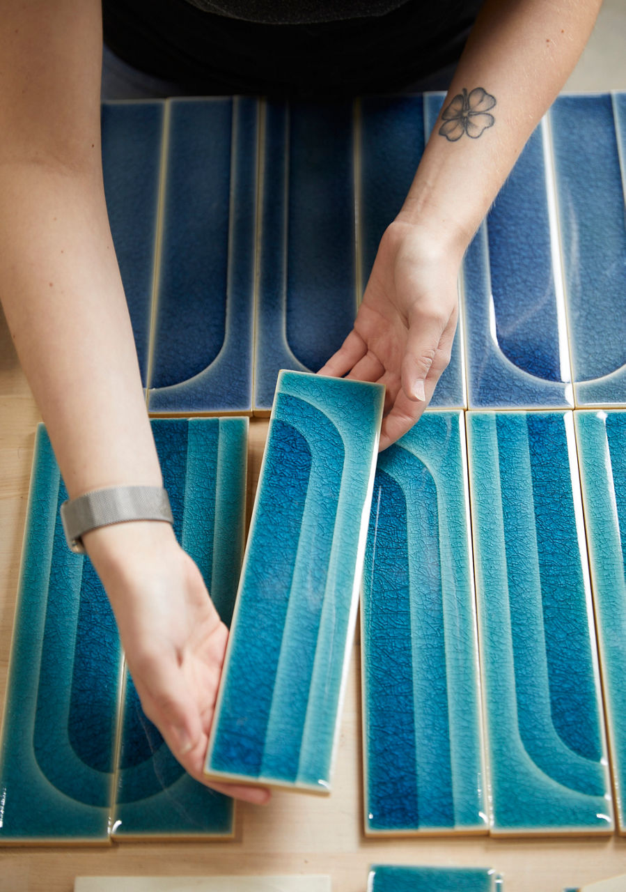 Close-up of hands arranging blue and white ceramic tiles from Kohler's WasteLAB, showcasing sustainable and recycled tile design.