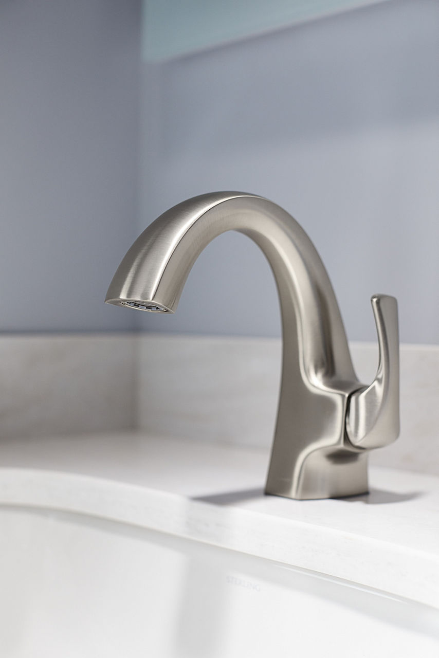 A brushed nickel bathroom faucet on a white counter with gray walls behind it.