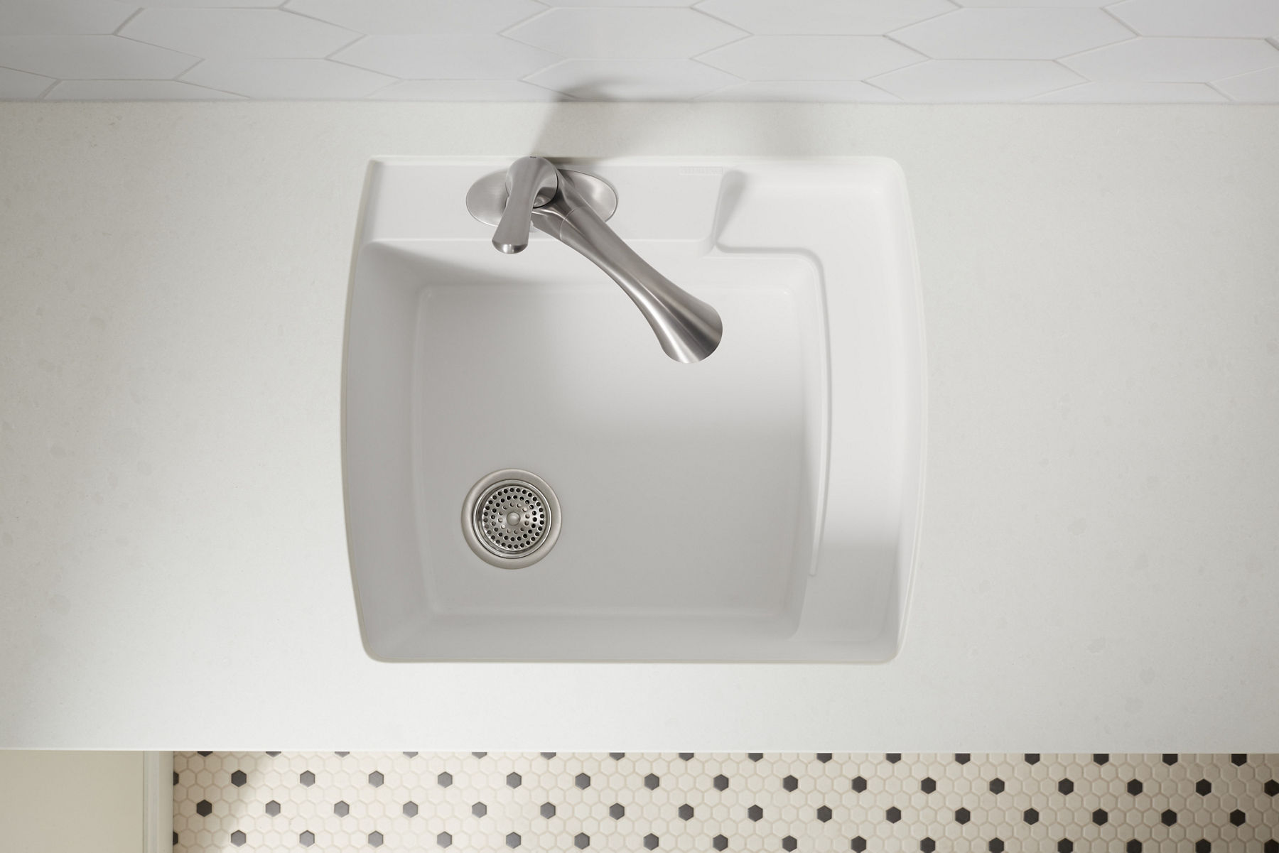 A stainless steel bar sink in a white counter top with a chrome faucet.