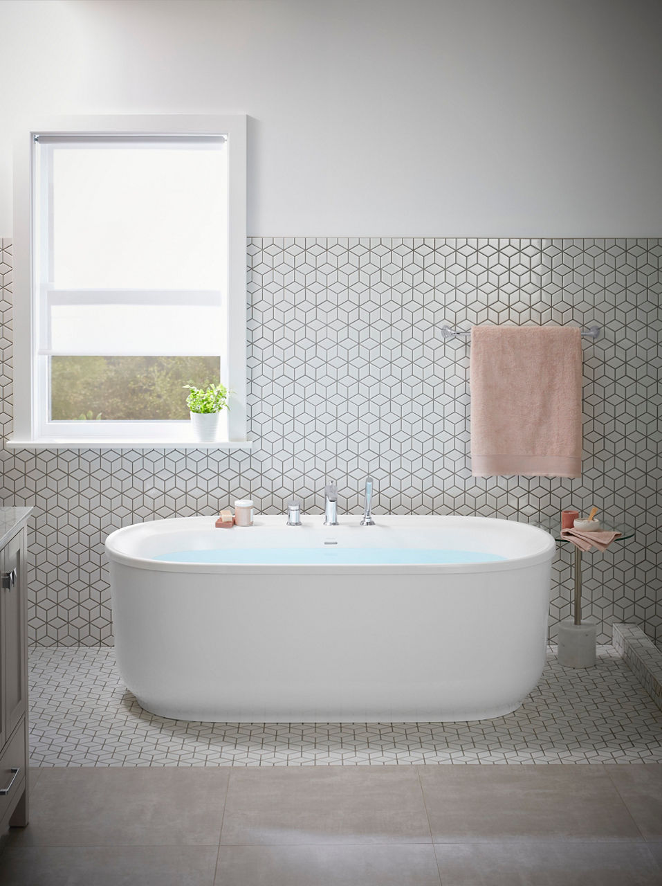 End detail of a freestanding bath in a room with geometric patterned white tile on the floor and wall.