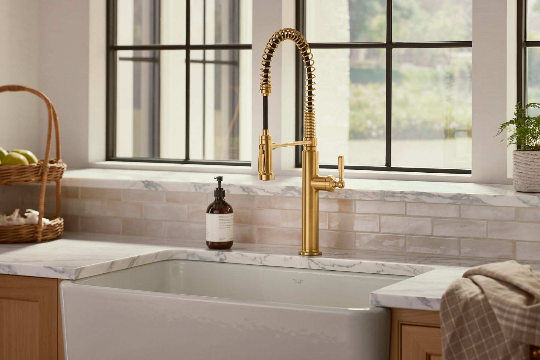 A brushed brass kitchen faucet on a marbled gray counter top above a mint green kitchen cabinet.