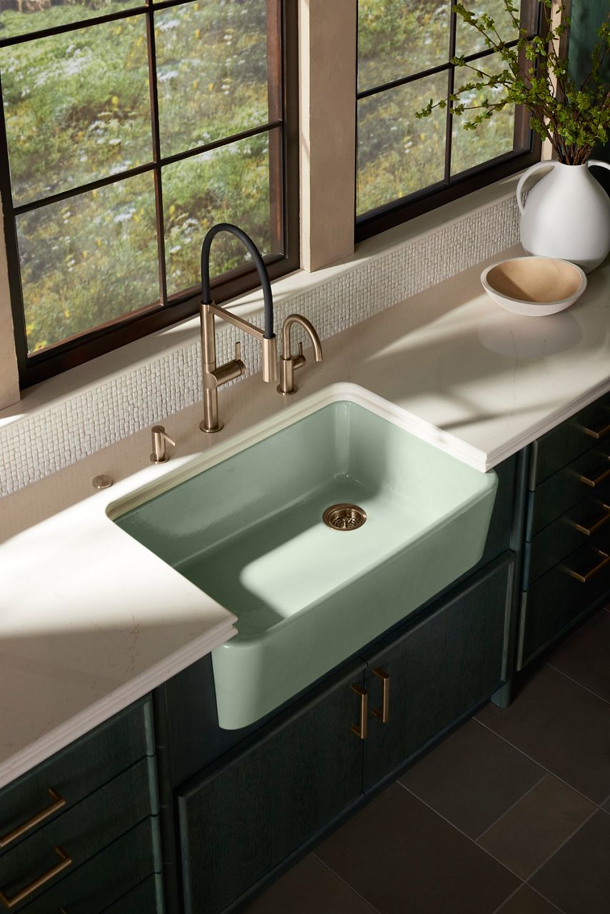 White apron-front sink under a window in a dark cabinet kitchen