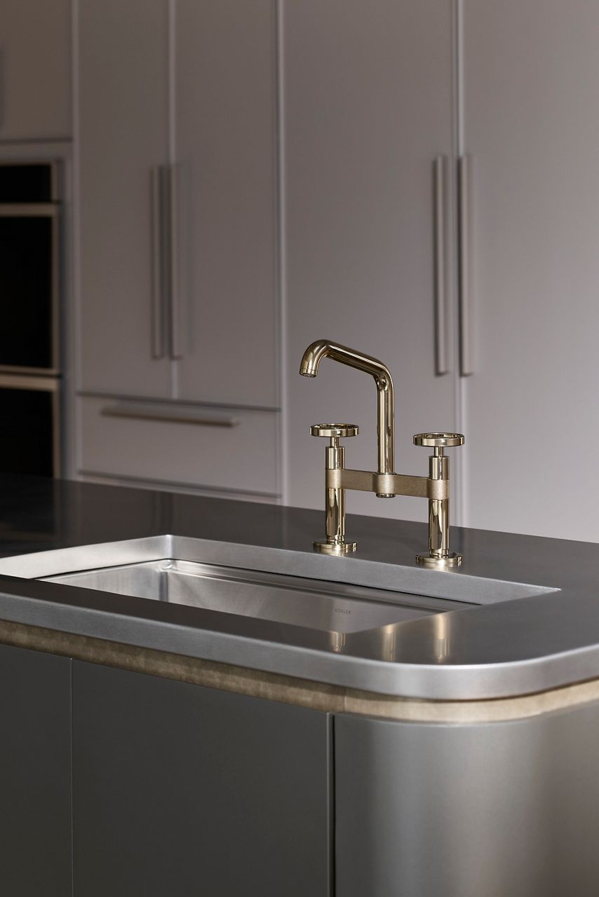 Close-up of a brass gold kitchen faucet with a dual handle design on a stainless steel sink
