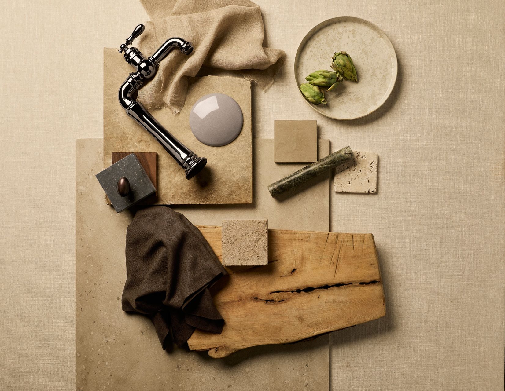 Chrome faucet styled with ceramic tiles, fabric swatches, and decorative objects on a beige background.