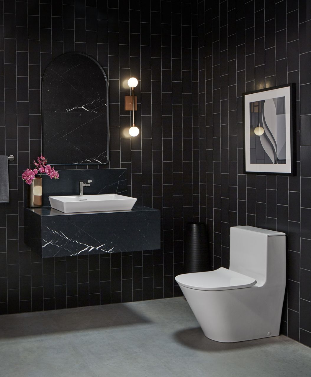 A white KOHLER Brazn one-piece toilet in a bathroom with black vertical subway tile walls.