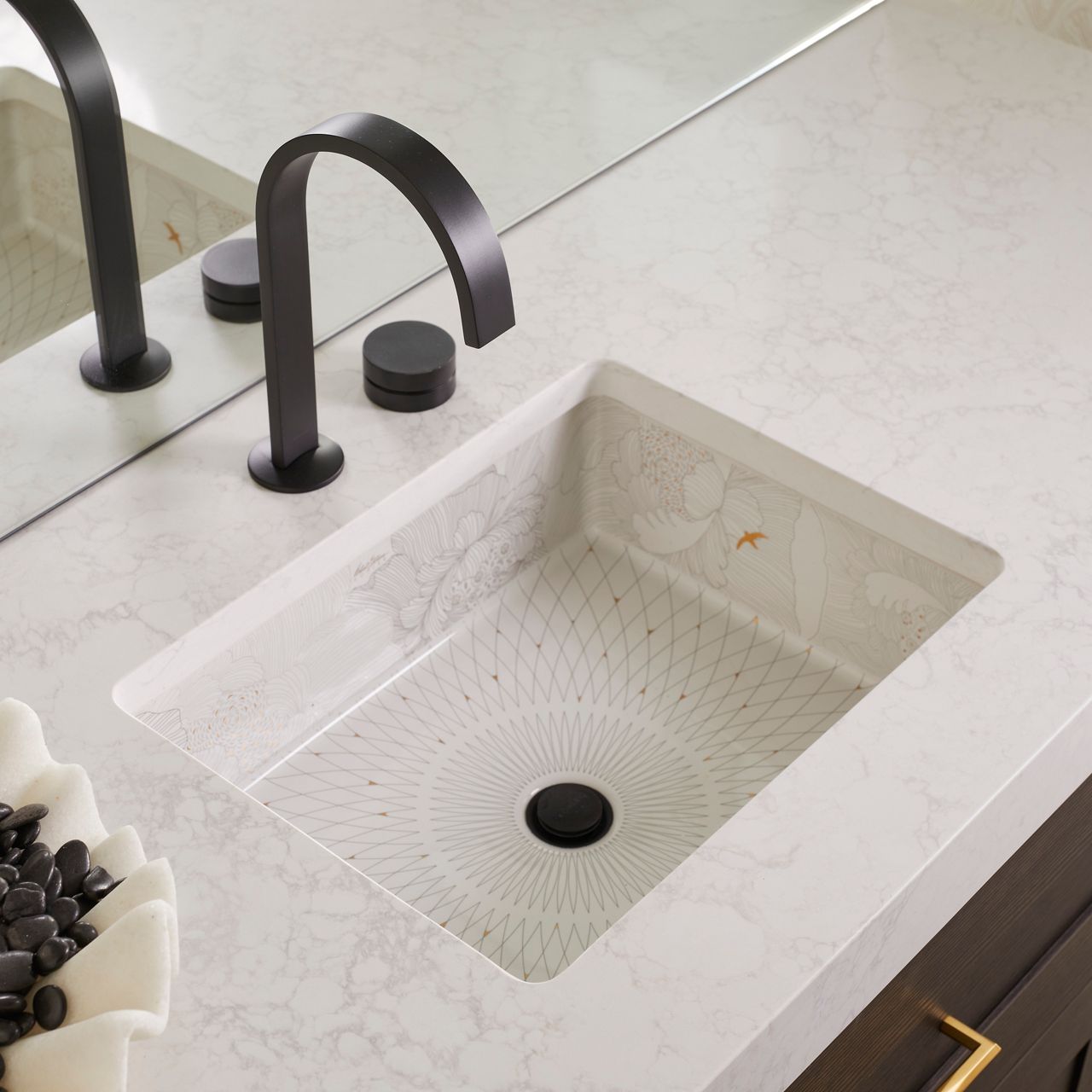 Decorative rectangular sink with etched floral pattern paired with a matte black faucet on a white marble countertop.