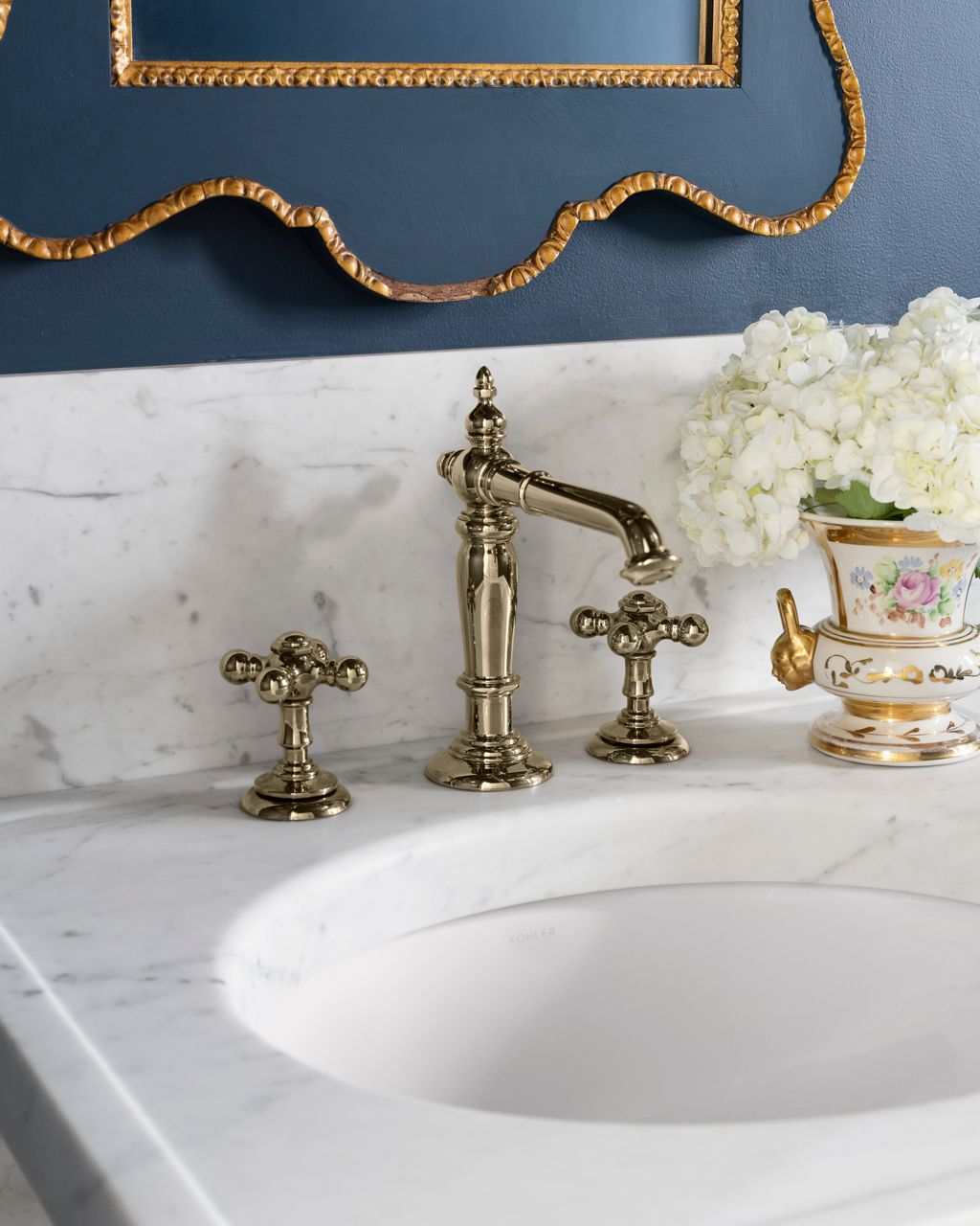 Classic white marble vanity with vintage-style brass faucet and decorative mirror against a deep blue wall.