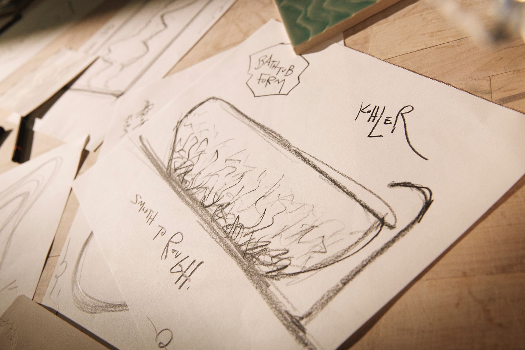 Close-up of a hand-drawn sketch depicting a bathtub design labeled 'Bathtub Form' with the description 'Smooth to Rough.' A green ceramic tile sample is partially visible in the corner, suggesting design inspiration.