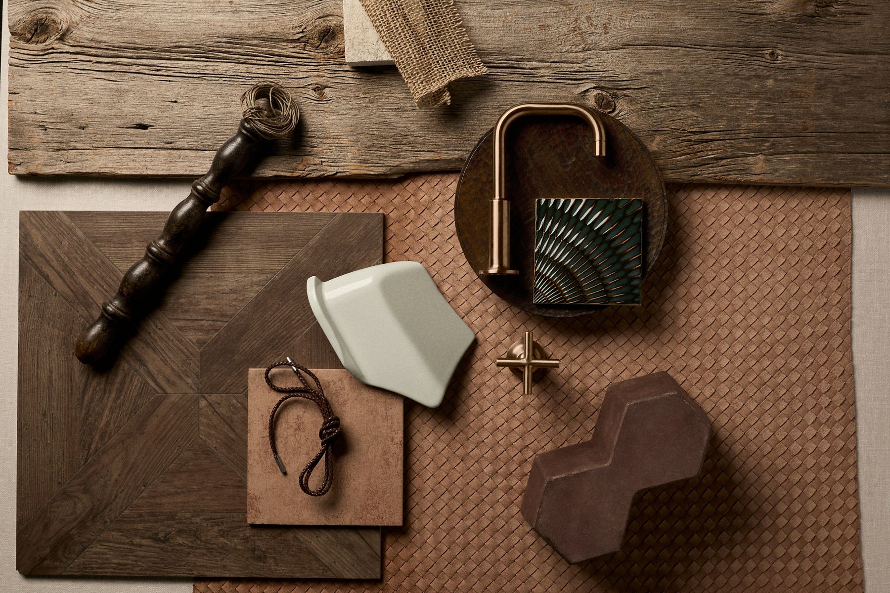 Flat lay of bronze faucet components with ceramic tile, leather accessories, and rustic textures.