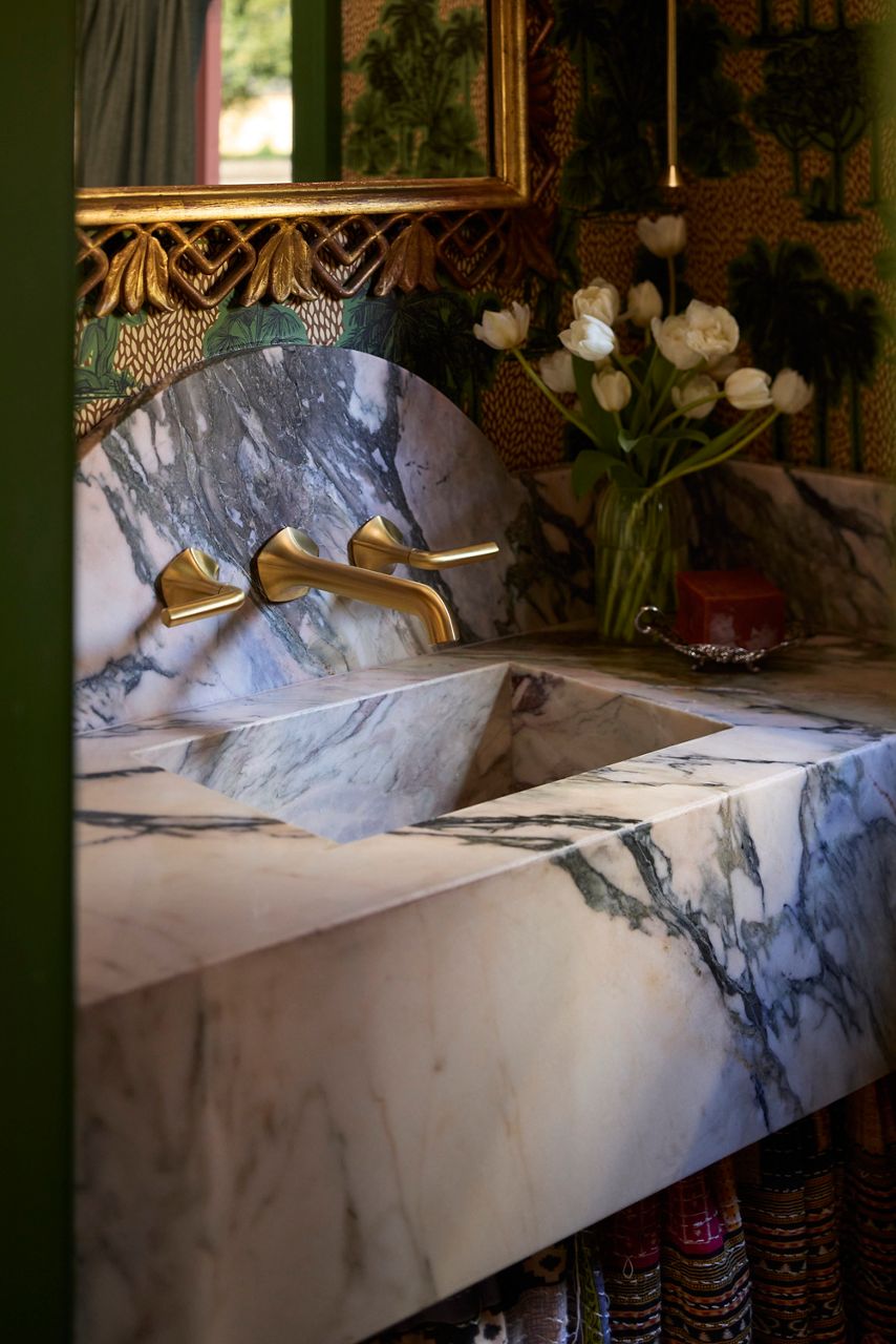 Sculptural marble vanity with integrated sink and brass wall-mounted faucet in a moody, richly decorated powder room.