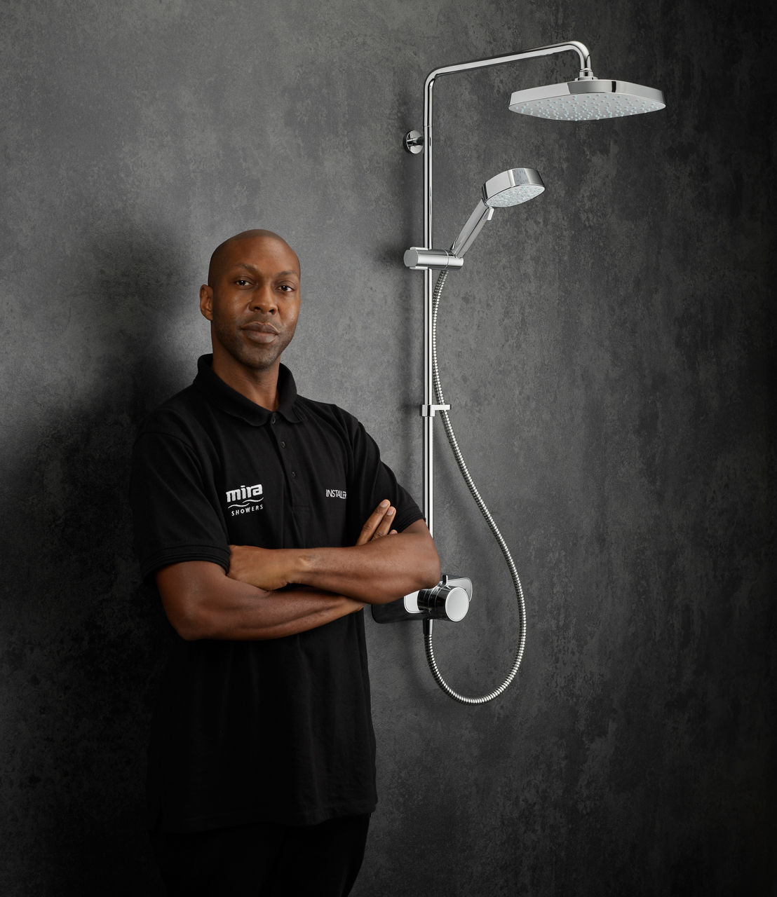 Installer stands with his arms folded in front of a textured grey wall, with a dual chrome Form shower to his right.