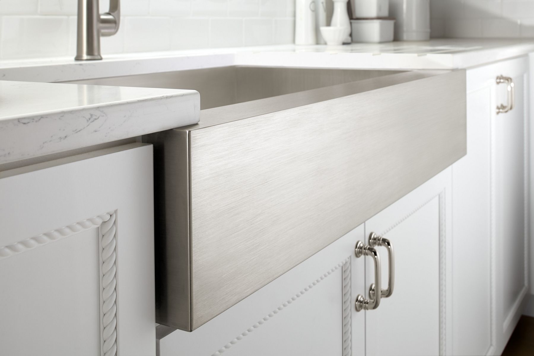 A kitchen with white cabinets and an aprong front stainless steel sink with a stone insert in the apron face.