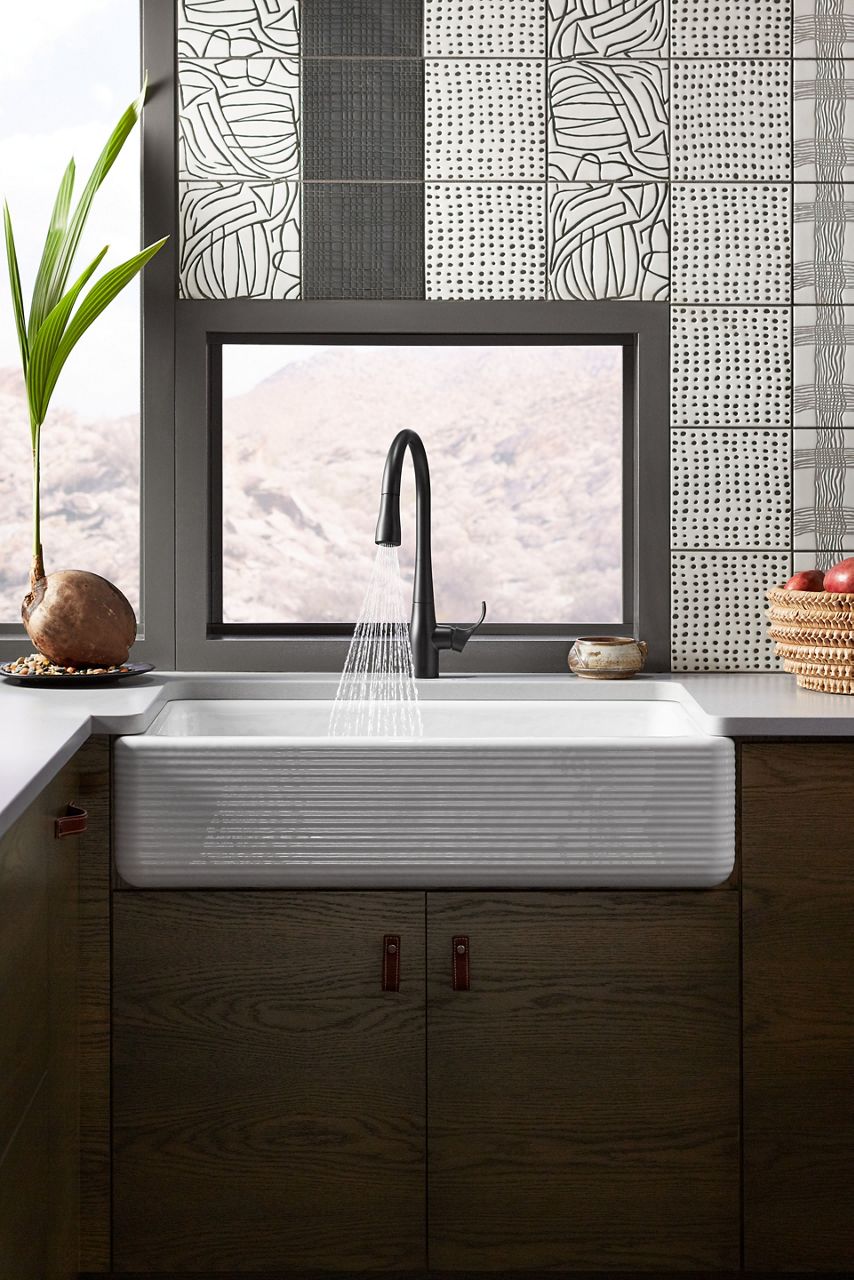 A kitchen with natural wood grain cabinets and a white farmhouse sink with horizontal lines engraved in the apron front of the sink.