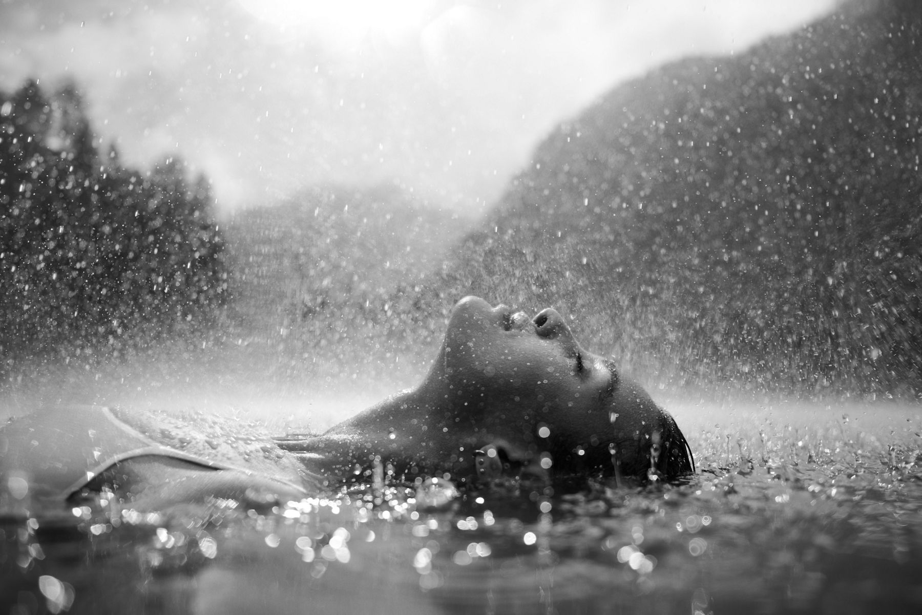 A woman floating in a pool of water with rain falling around her looking relaxed.
