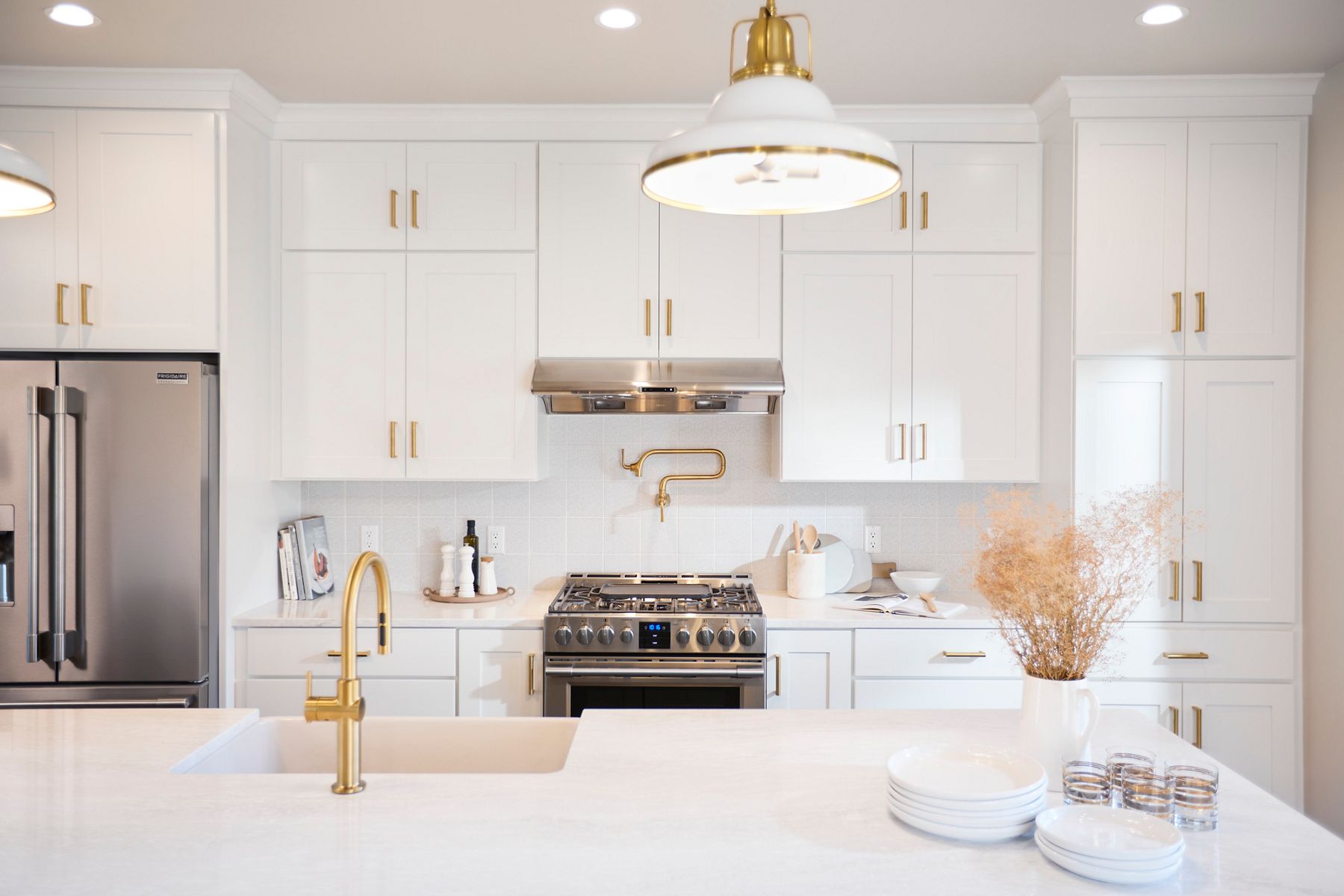 A kitchen all in white with brushed brass accents and stainless steel appliances.