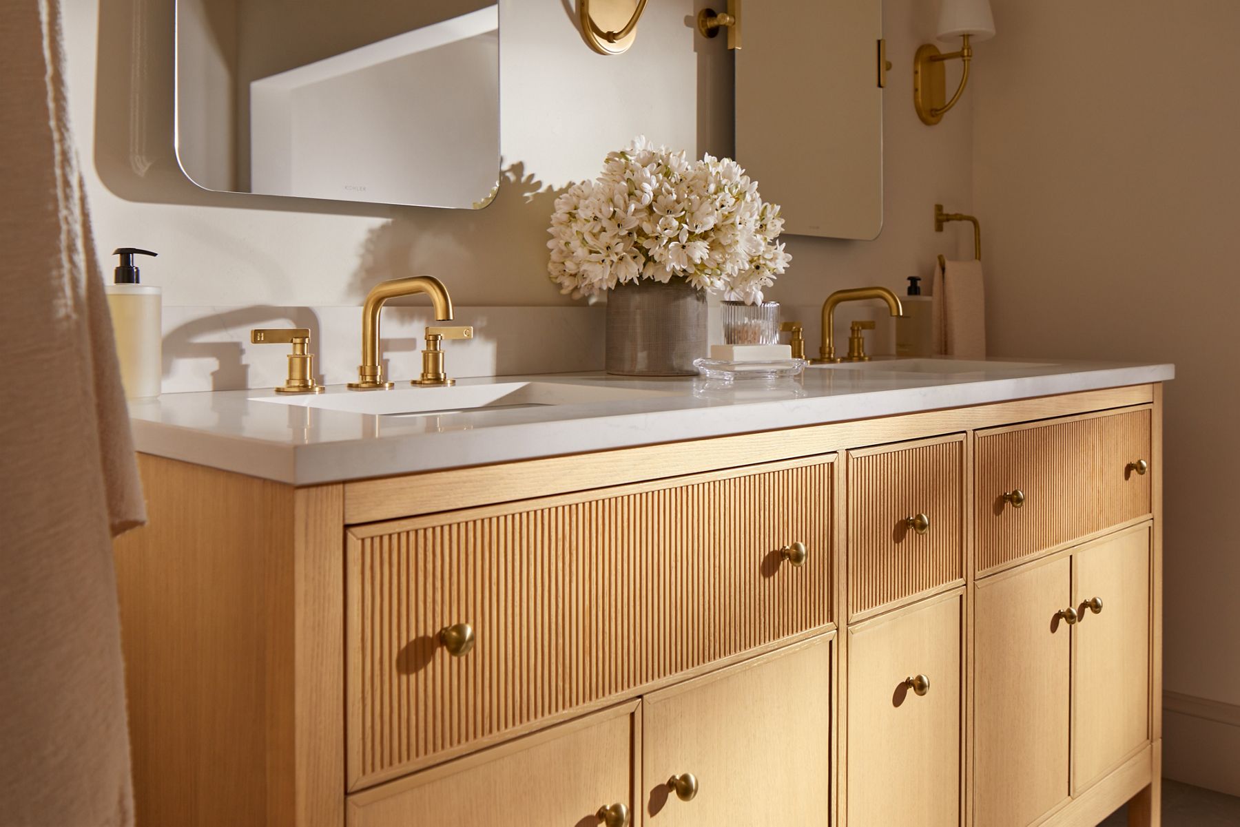 A bathrom vanity area in neutral tones with a wood double vanity, brushed brass faucets, and mirrors designed by Shea McGee.