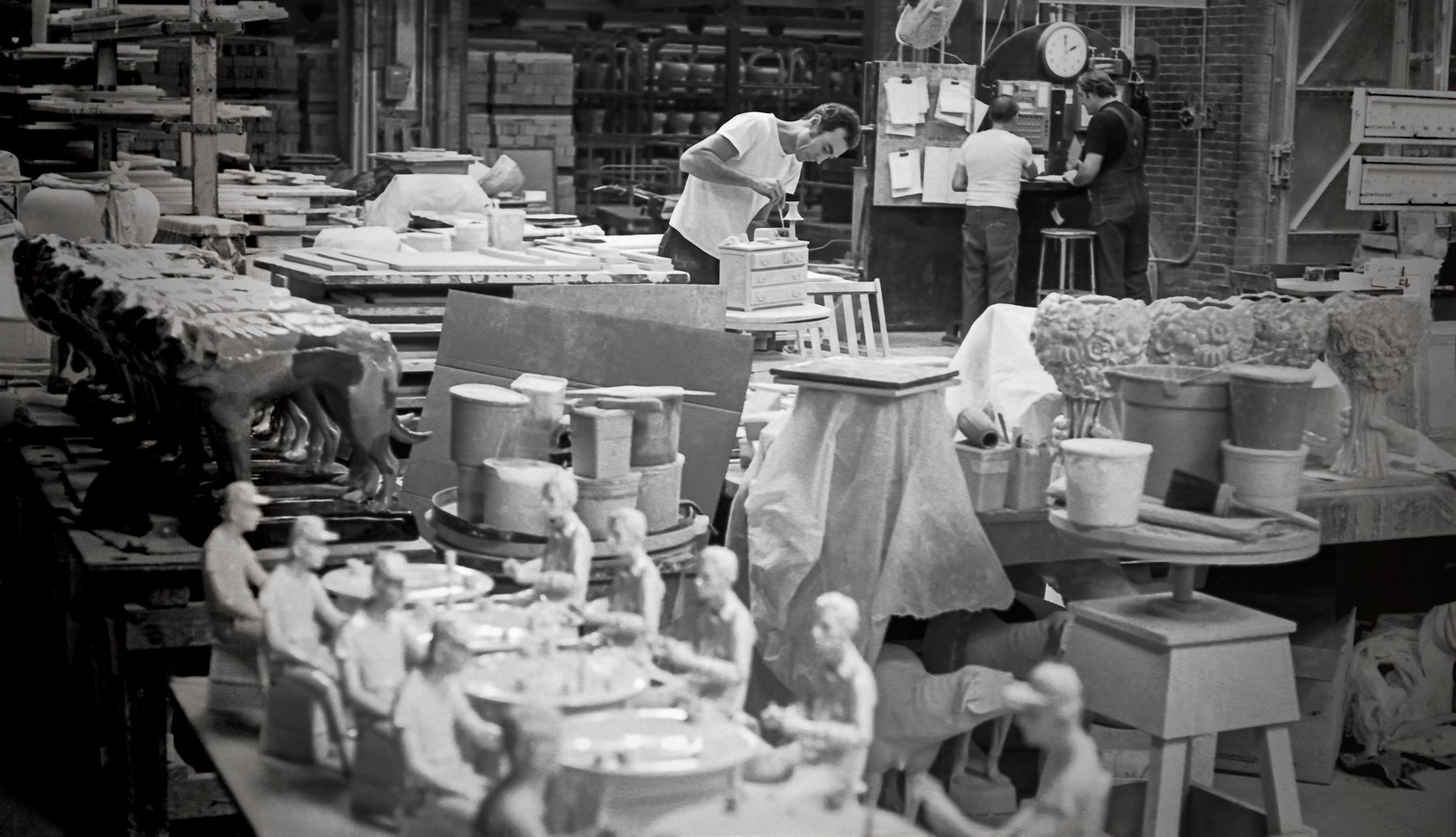 Archival image of Kohler artisans working in a ceramic workshop surrounded by clay pieces and molds.