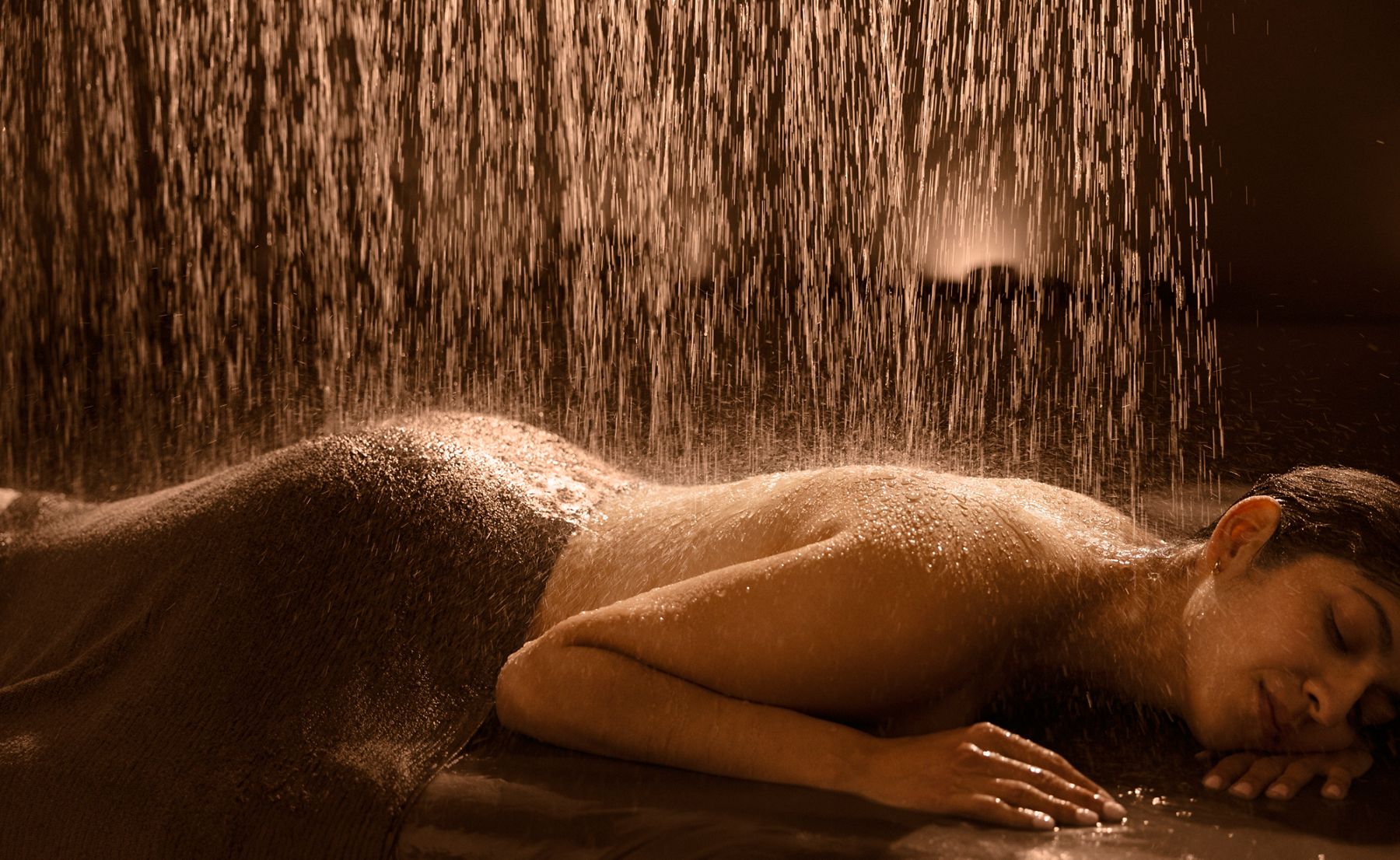 Person relaxing under a warm water shower, with the text 'A Wellness World Awaits' promoting immersive experiences in Kohler, Wisconsin.