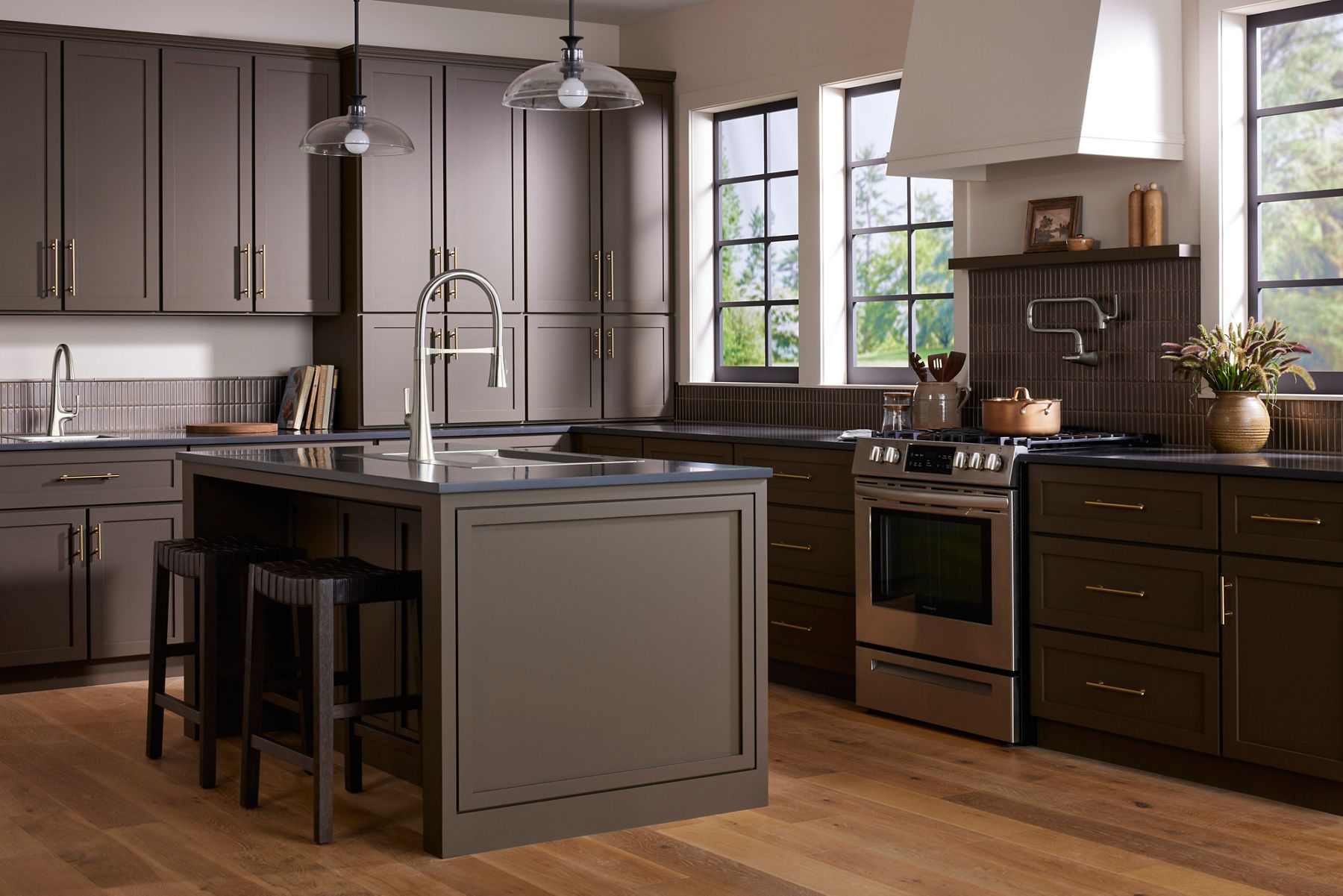 A modern kitchen in brown tones with a stainless steel oven and KOHLER kitchen sink and faucet.
