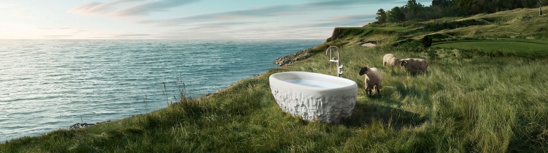 Outdoor scene with a sculptural bathtub from the Kohler x Arsham Landshapes Collection placed on a grassy cliff overlooking the ocean.