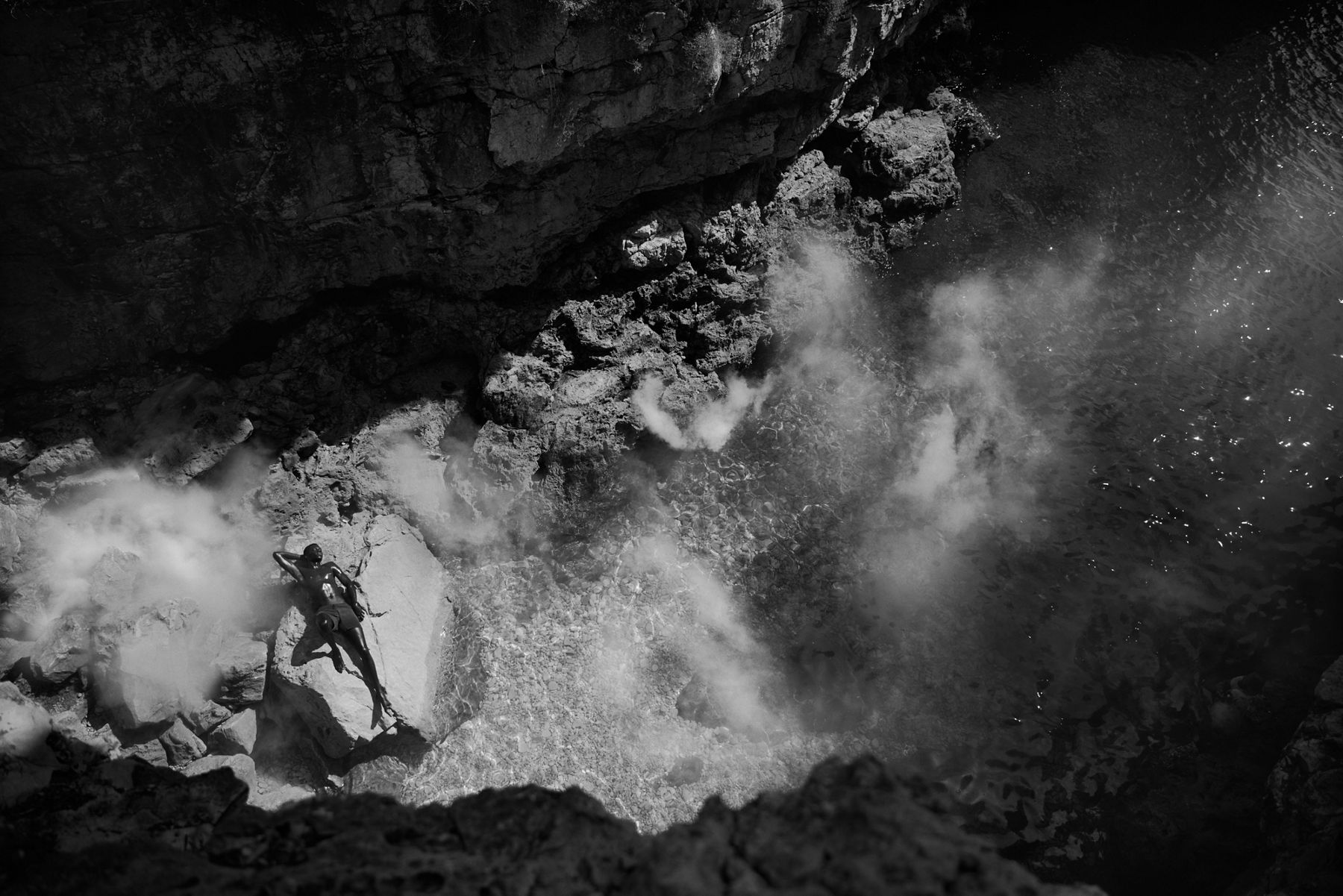 Black and white image of a person relaxing on rocky terrain near misty water, with the text 'Personalize Your Escape' promoting precise shower control at your fingertips.