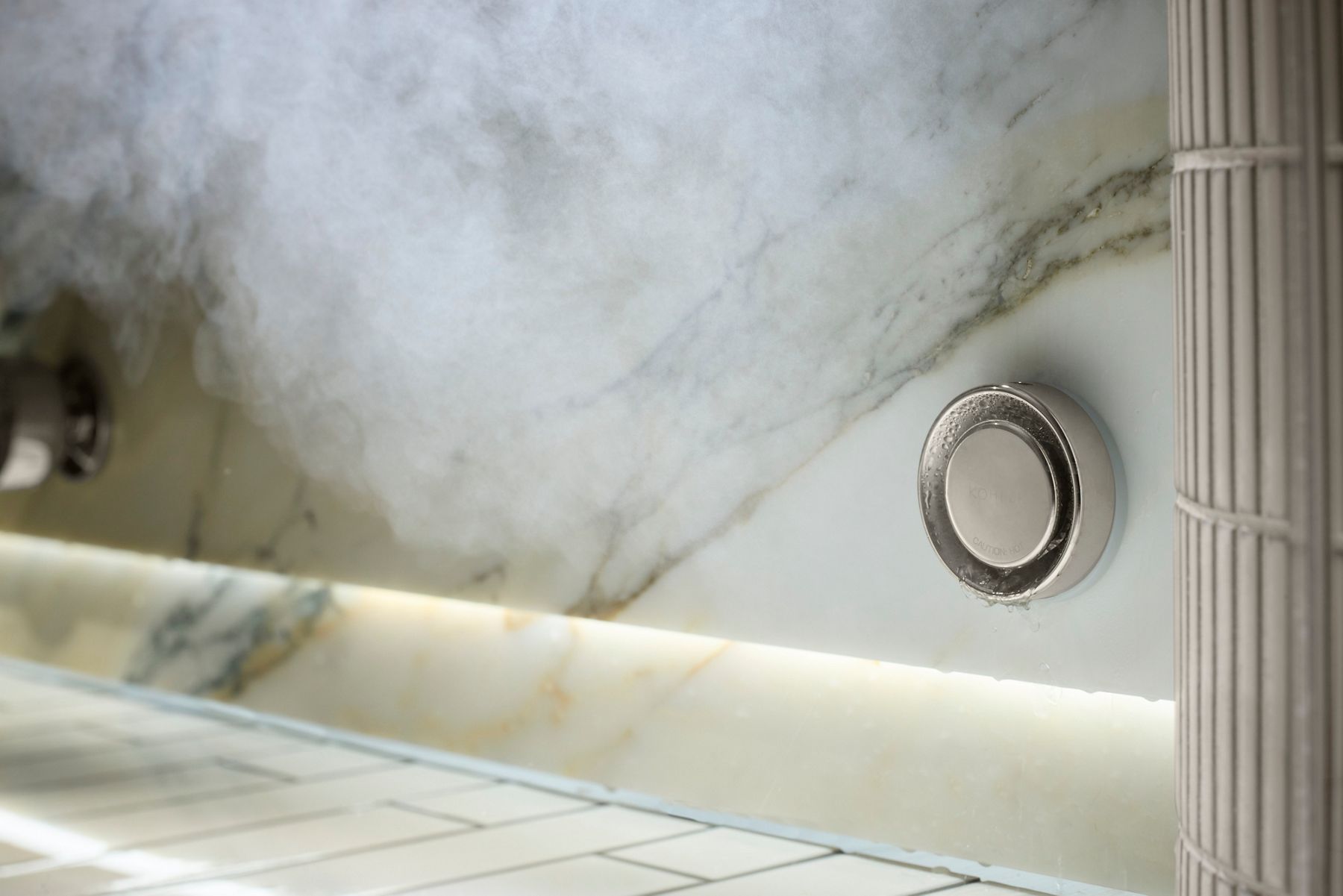 Close-up of a sleek steam control button on a marble wall, with mist rising and the text 'Through the Mist' encouraging steam-enhanced routines.