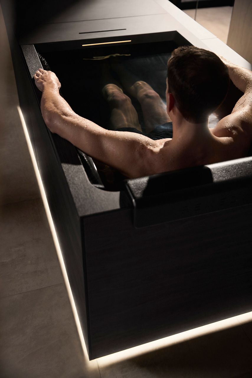 A man sitting in a Kohler Ice Bath in a serene, dimly lit room.