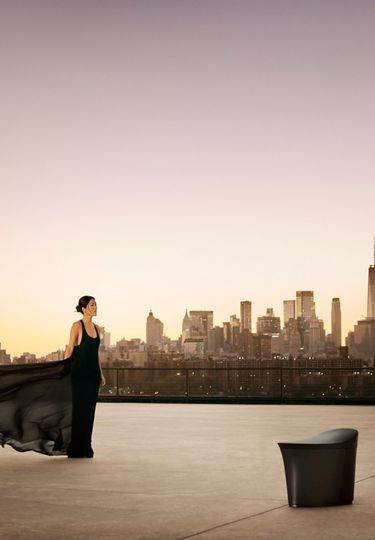 Laura Kim stands in a flowing black chiffon dress, accentuating the curved design of the Veil smart toilet against the New York City skyline.
