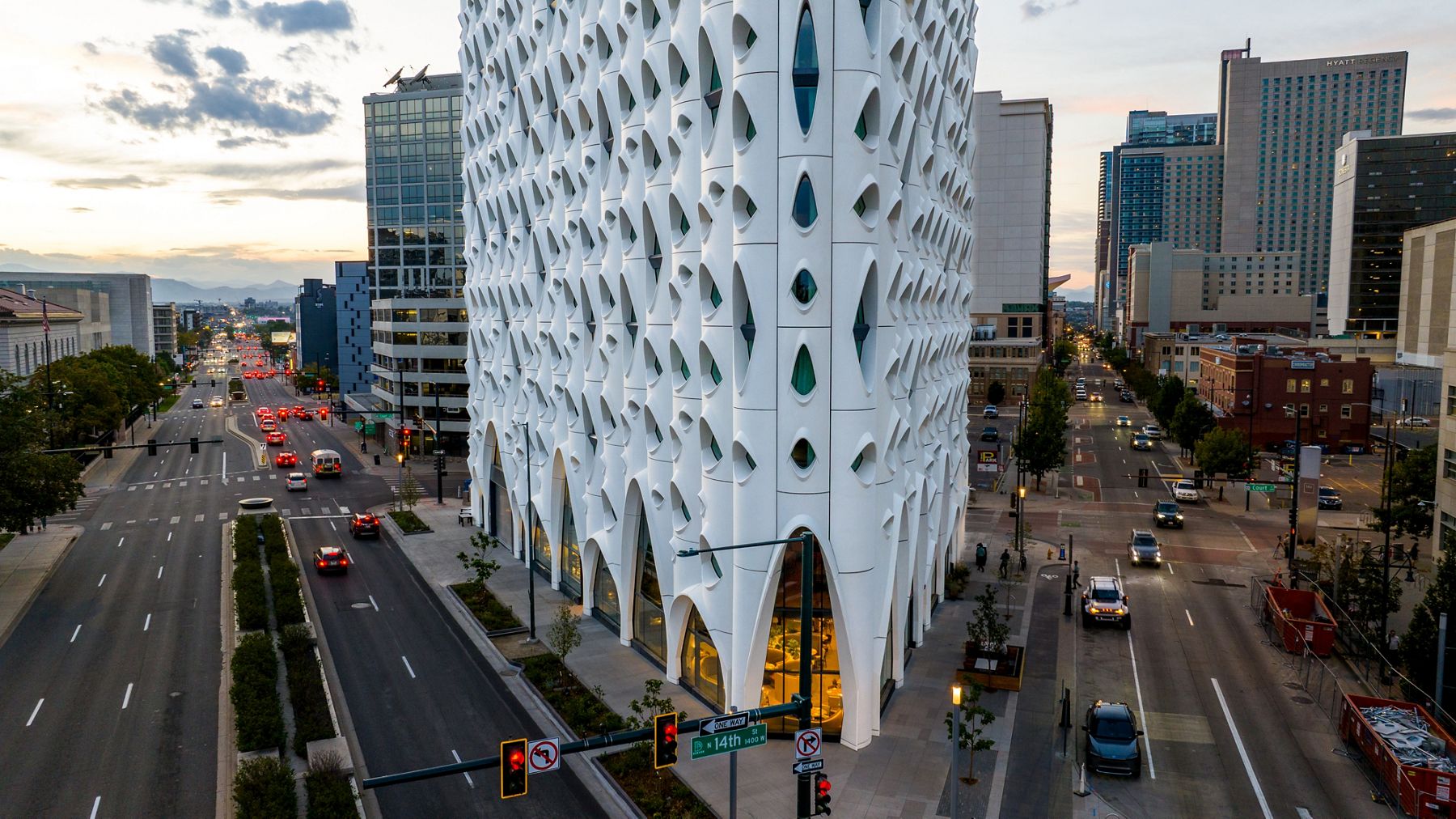 Street view of a modern white geometric-designed building with city traffic and urban skyline.
