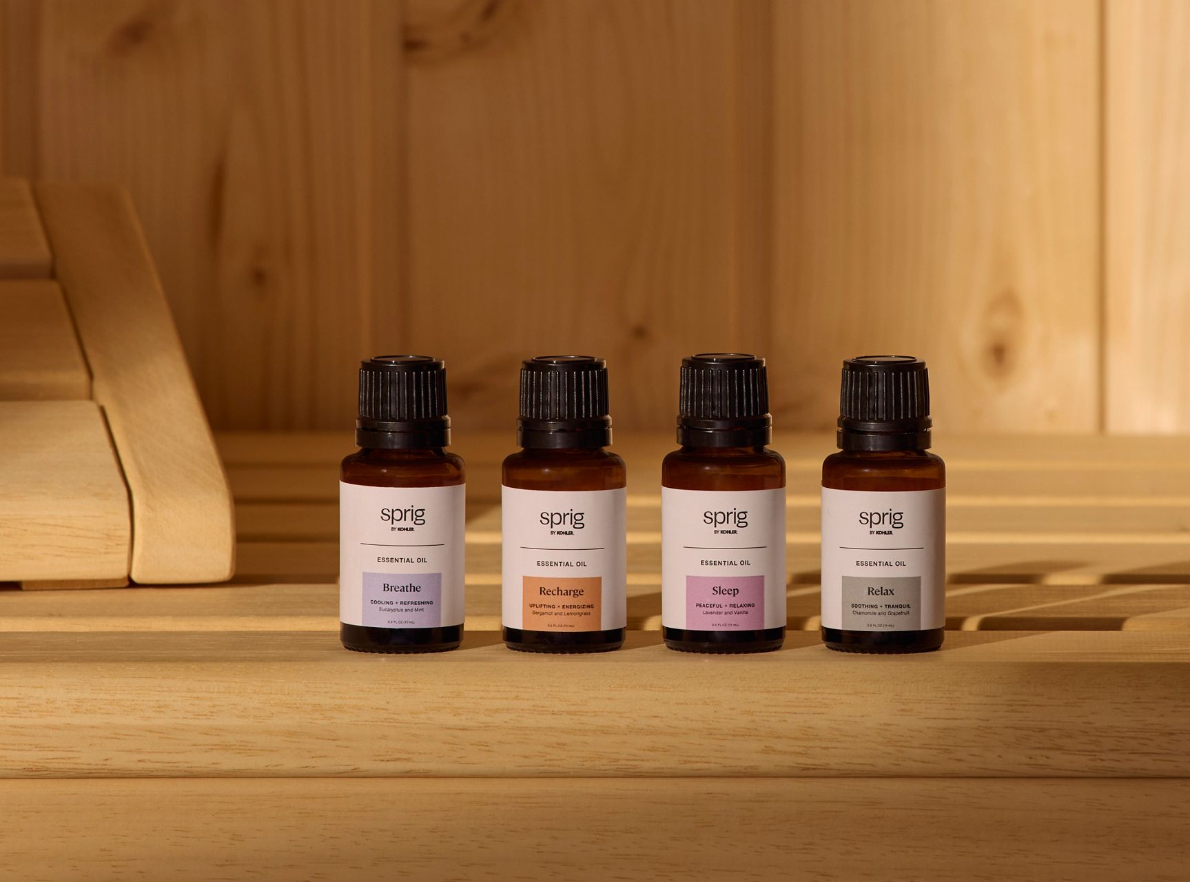 Close-up off our essential Oil bottles with black caps and labeled fronts, displayed on light wood.