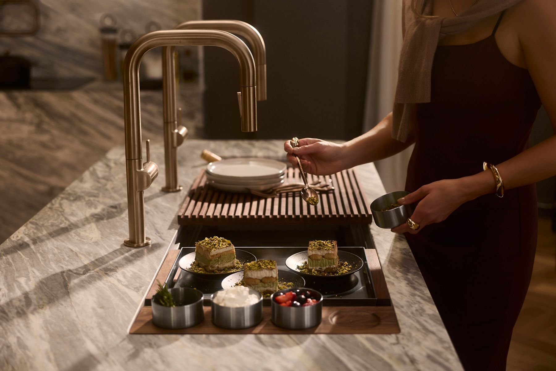 Woman adding the finishing touches to her meal alongside two pull down faucets in a warm, neutral kitchen.