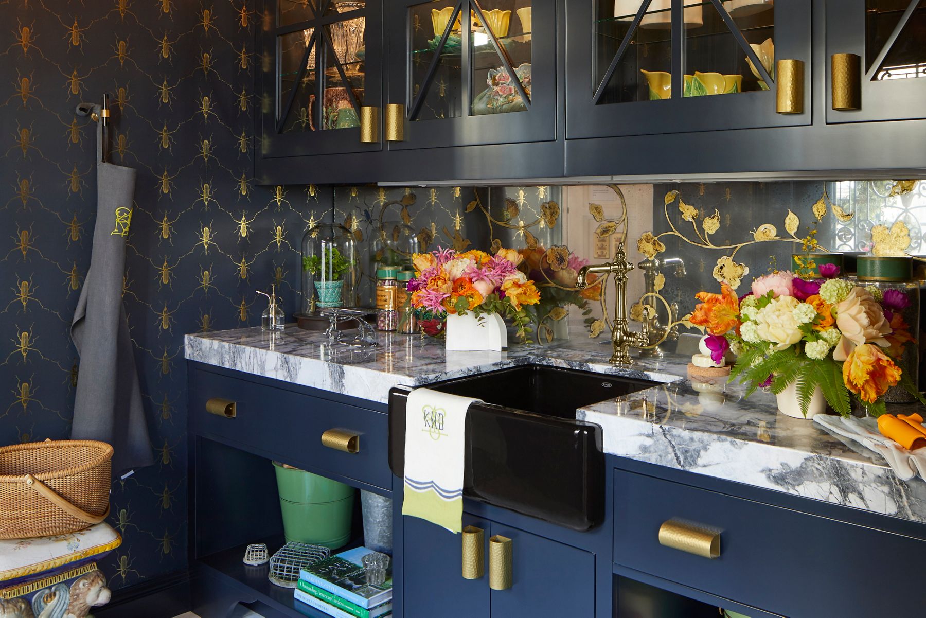 A bold and vibrant wet bar area with indigo cabinets and wallpaper with brushed brass hardware and gold accents, and a faucet finished in polished nickel.