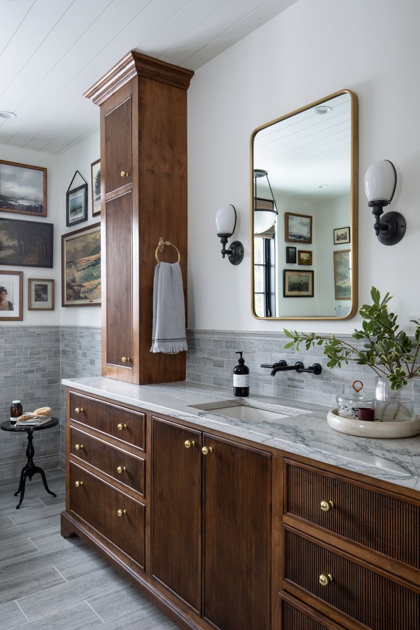 A bathroom with classic design features tiled backsplash, KOHLER wall-mounted widespread faucet with lever handles in Matte Black, marble vanity top, and a vanity and linen cupboard with traditional trim and fluted details.