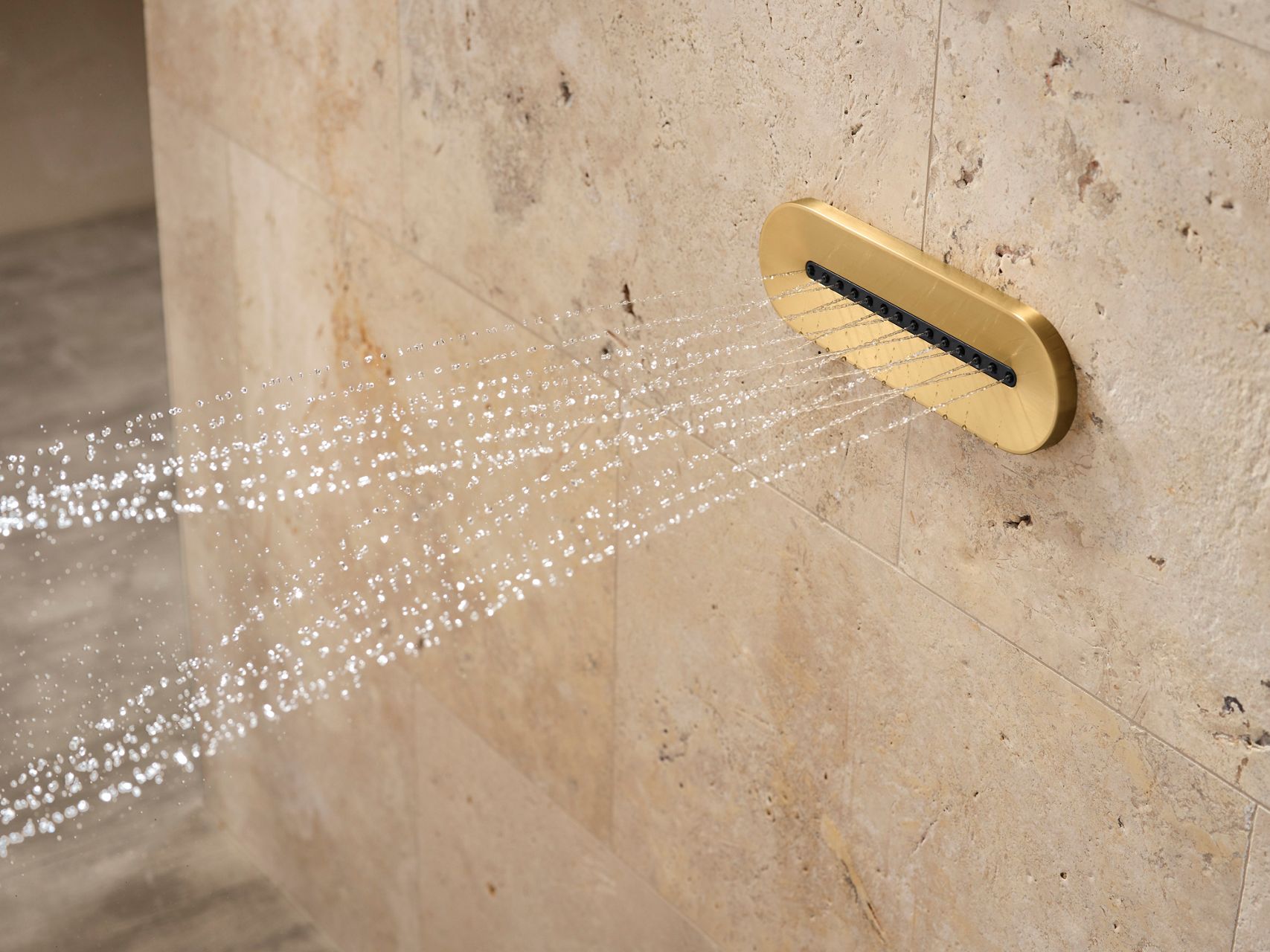 Un jet de douche en laiton moderne contre un mur carrelé en pierre beige, pulvérisant des jets d’eau fins en angle, mettant en lumière un accessoire élégant et luxueux de la salle de bain.
