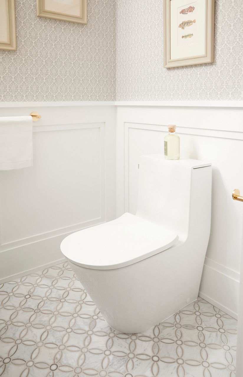 A one-piece toilet against a white framed wall with a white patterned tile floor.