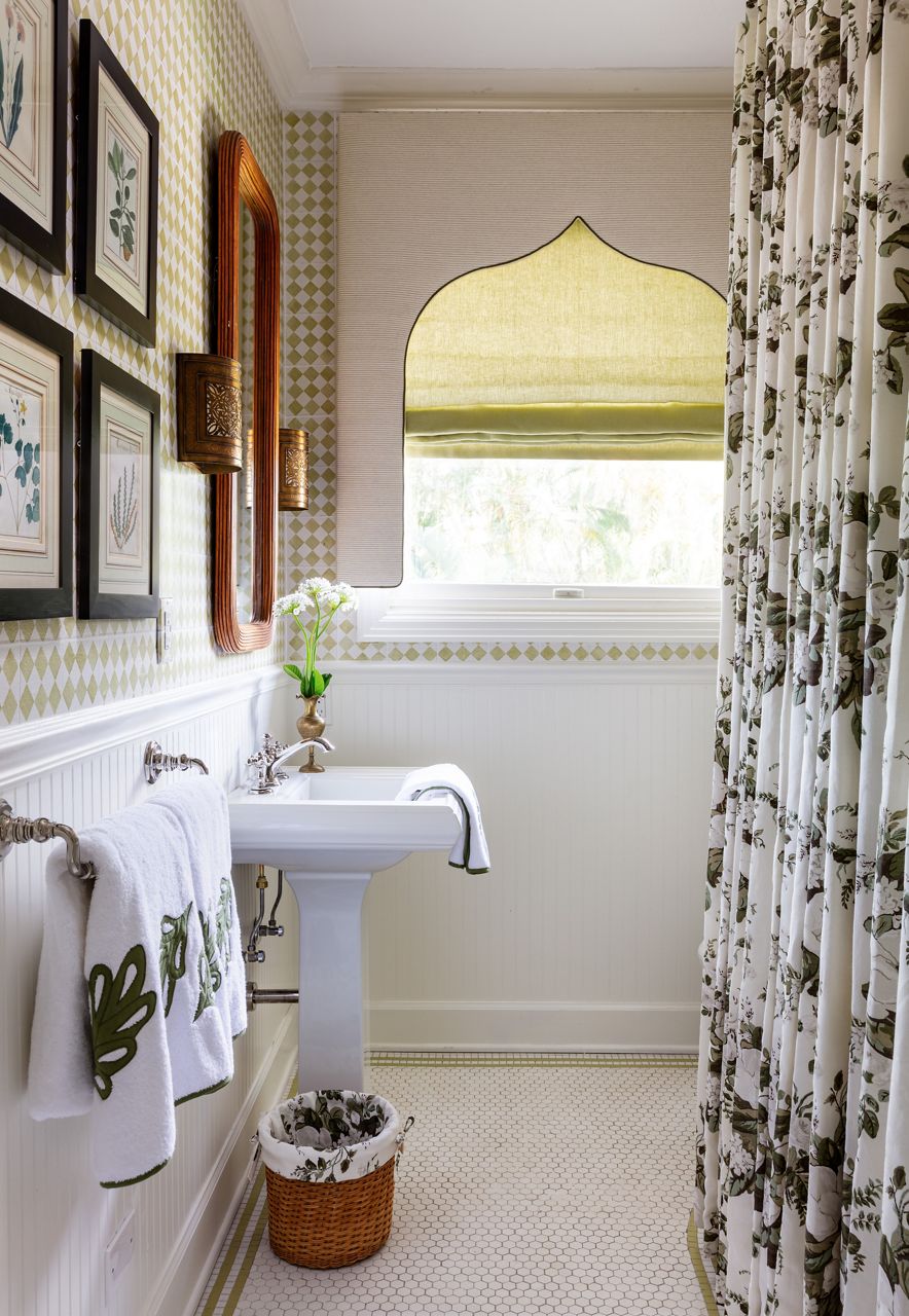 A bathroom with white KOHLER pedestal sink, black and white floral shower curtain, white towels with floral appliques, green and white gingham wallpaper above white beadboard, and framed artwork.