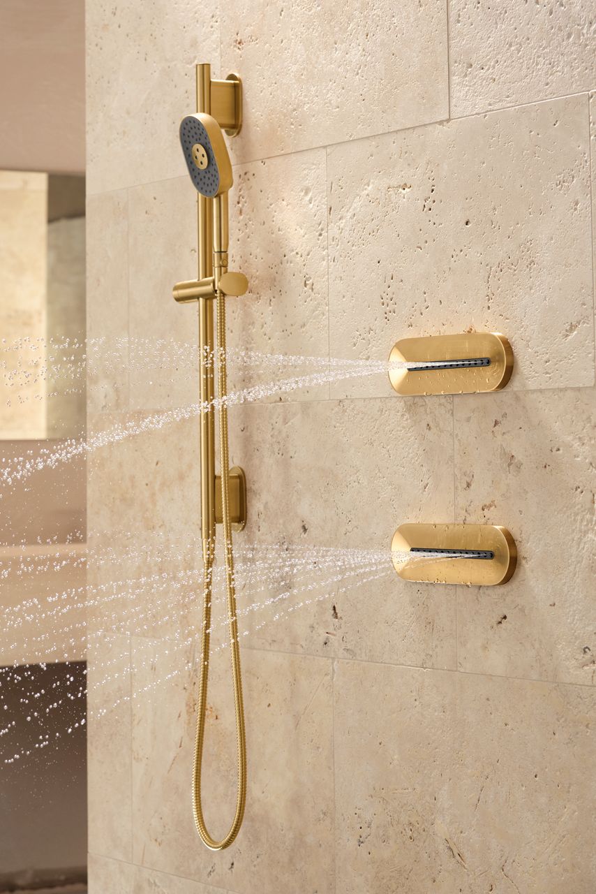 A shower with sand-colored walls, KOHLER Statement handshower, and oval body sprays.